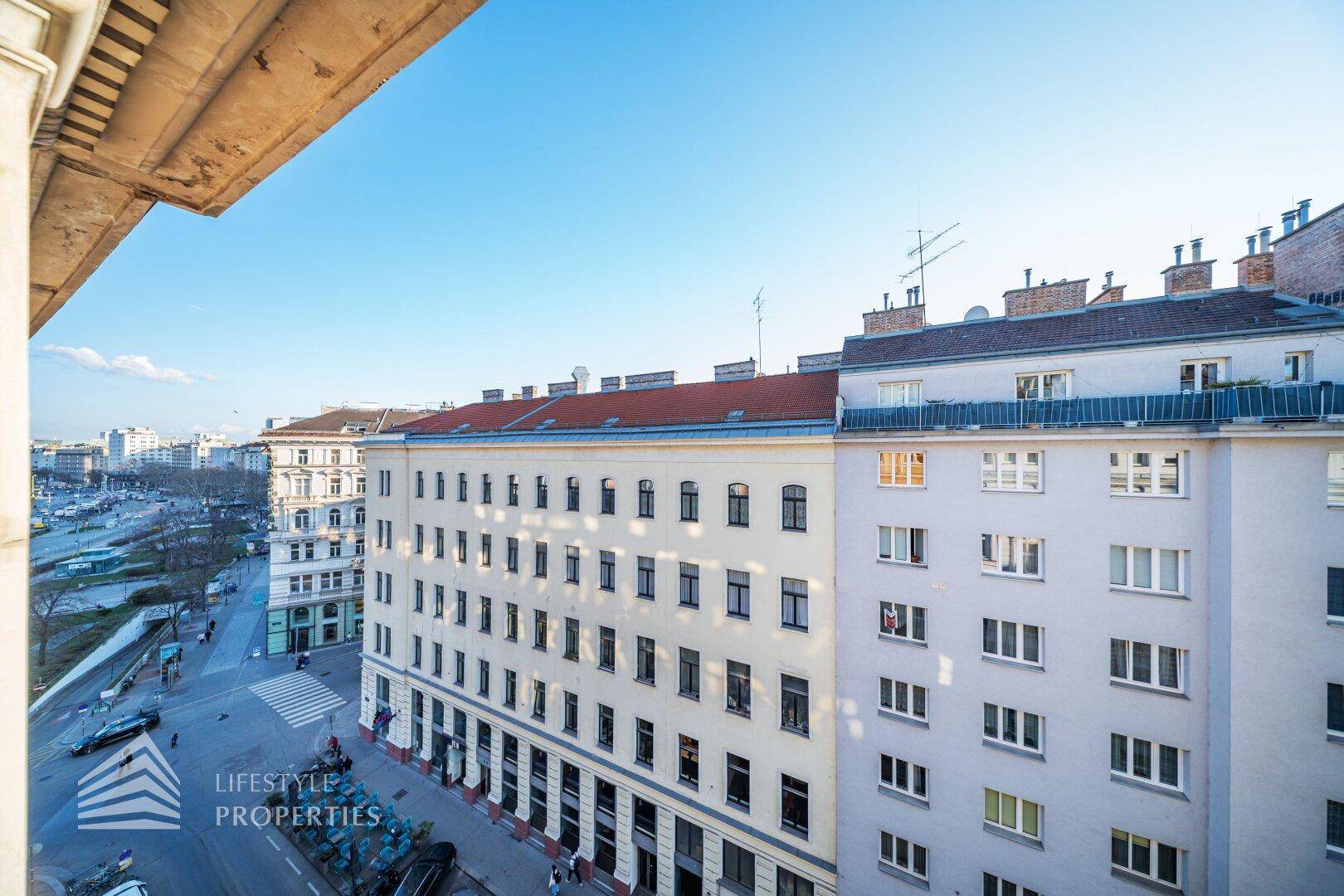 Panoramablick auf eine belebte Stadtstraße mit historischen Gebäuden unter blauem Himmel.