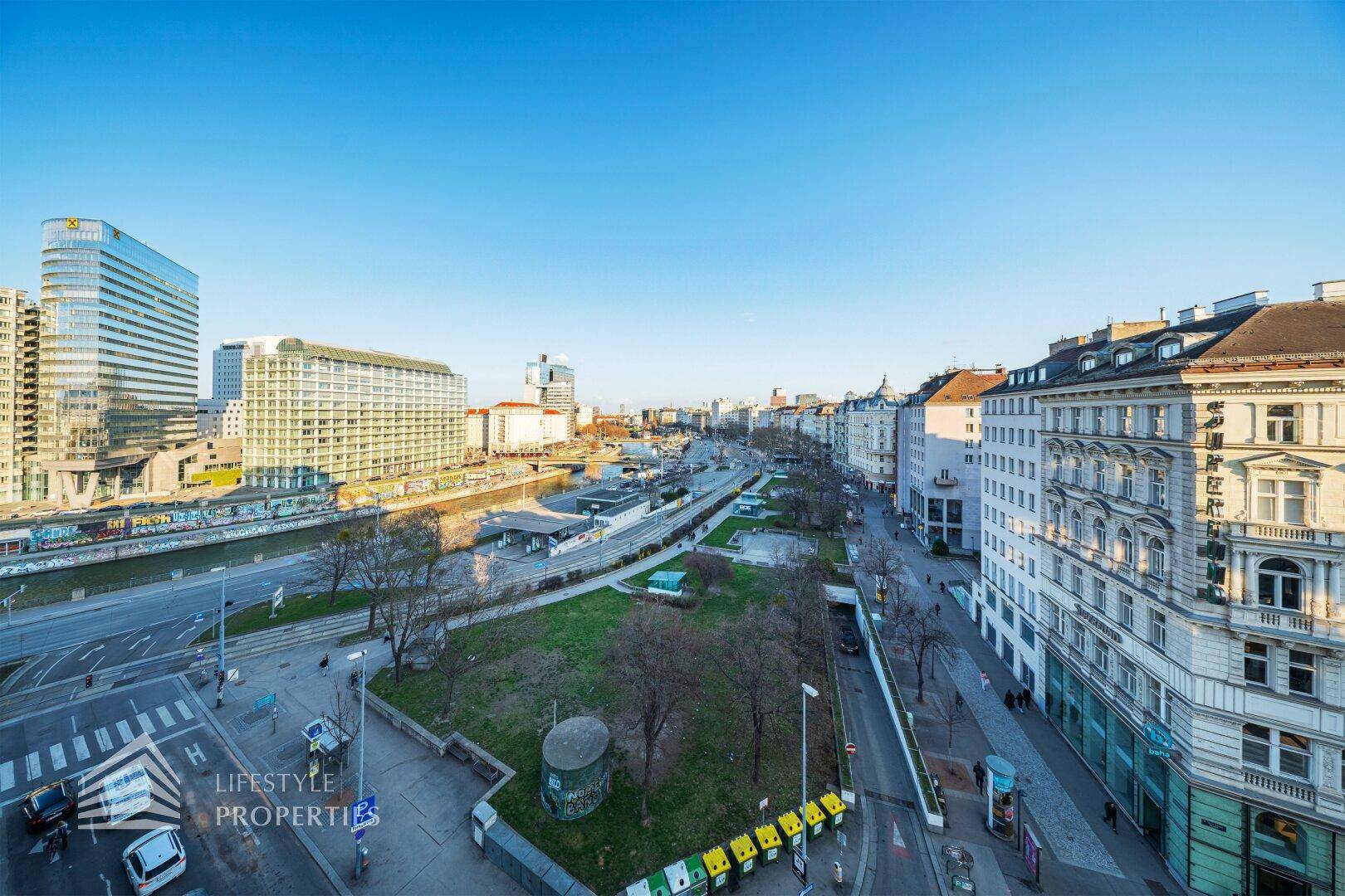 Weitläufiger Blick über eine belebte Stadtstraße mit modernen Gebäuden und einem Fluss.