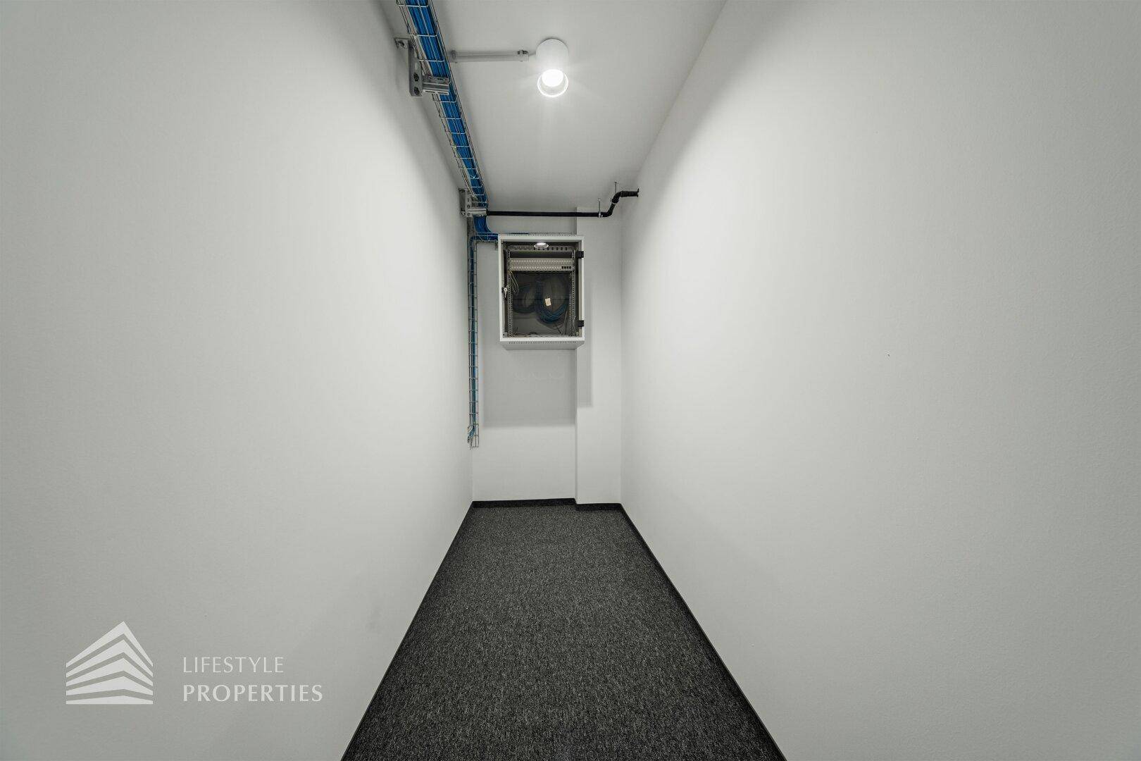 Schmaler Flur oder Abstellraum mit Teppichboden und sichtbaren Installationen an der Decke.