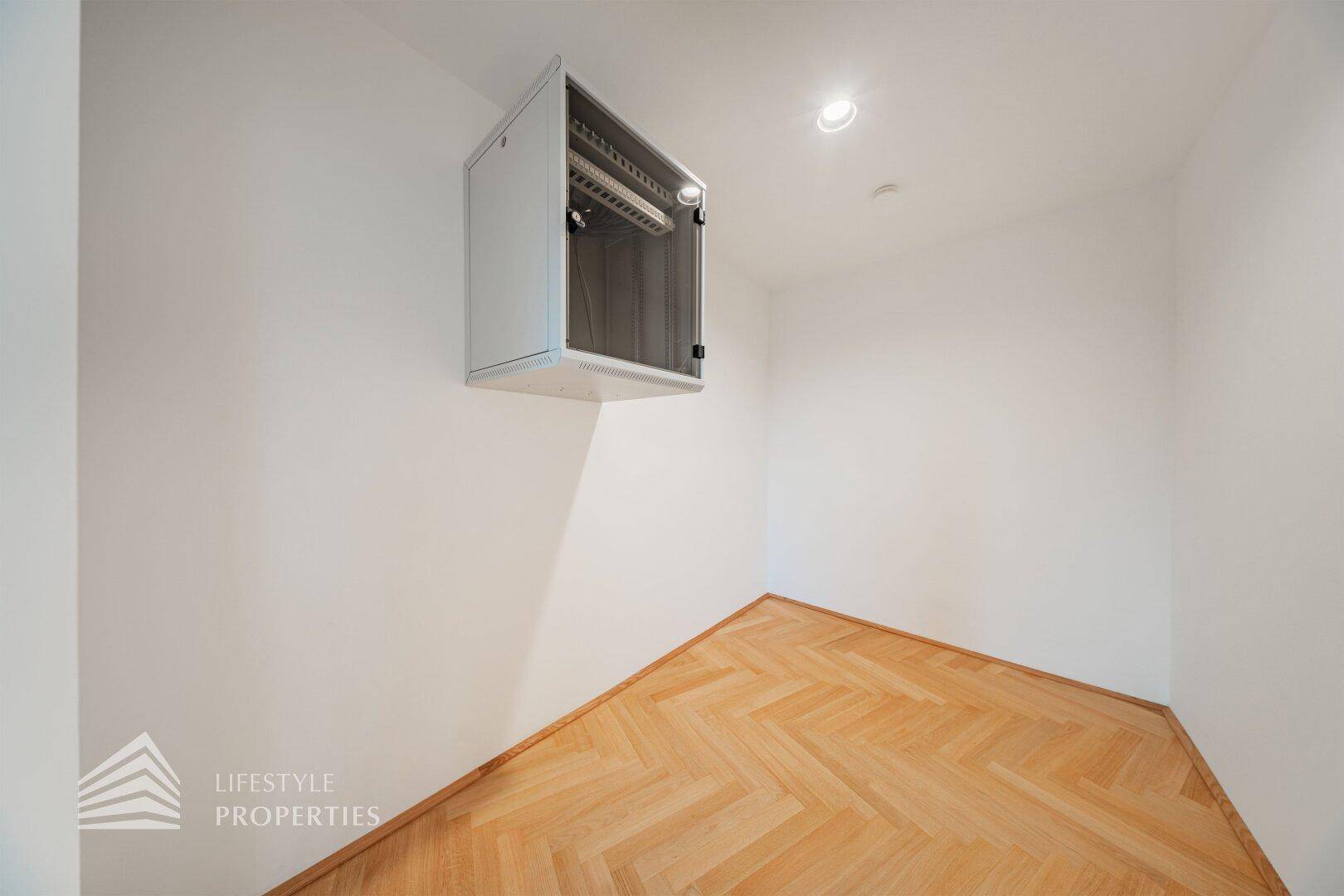 Kleiner Raum mit Fischgrätparkett und einem an der Wand montierten Serverschrank, ideal für Technik.
