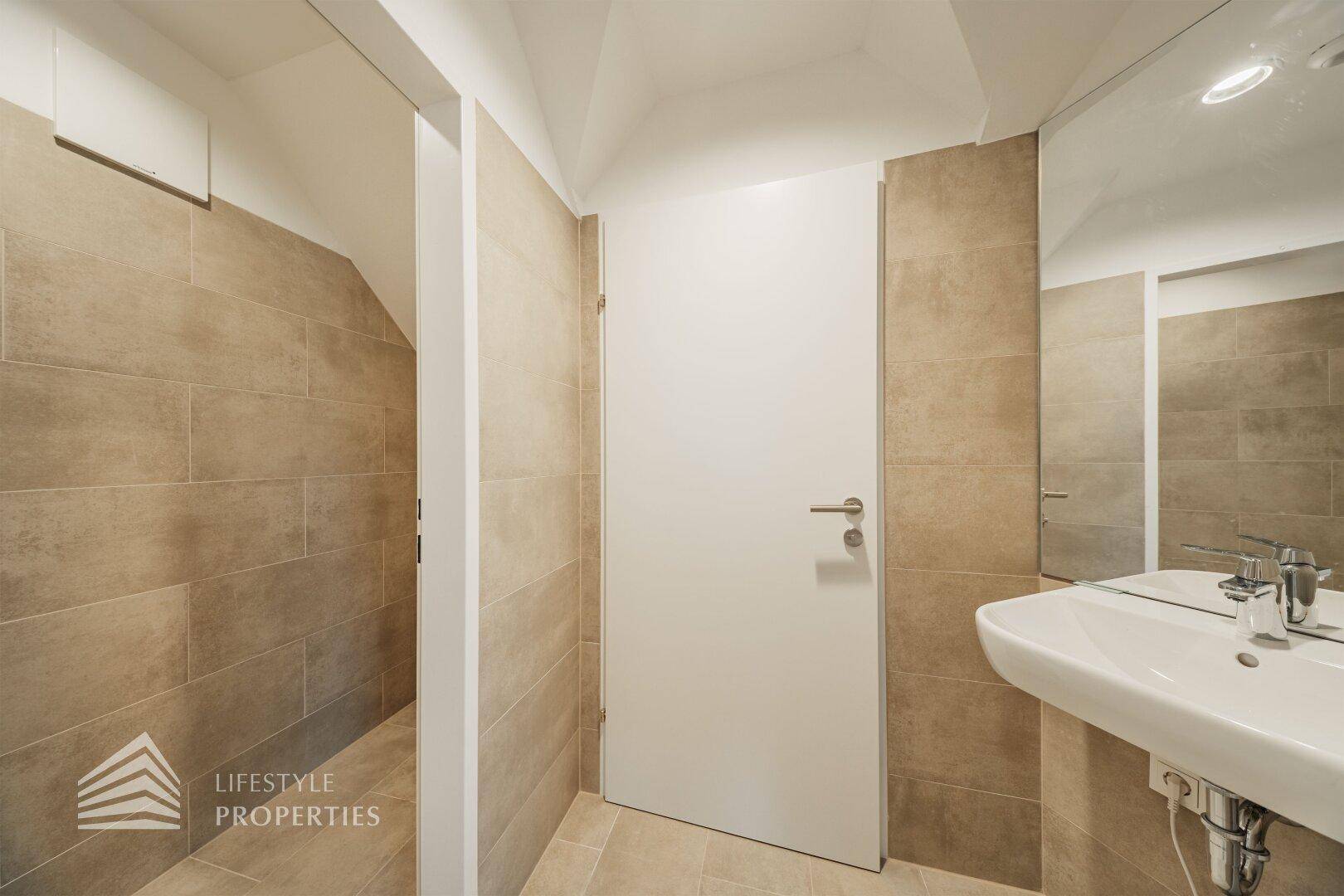 Modernes Badezimmer mit beigefarbenen Fliesen, Waschbecken und einem Spiegel, der den Raum optisch vergrößert.