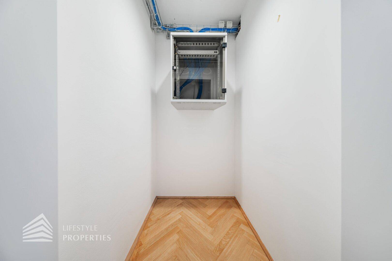 Kleiner Technikraum mit Holzboden und einem an der Wand montierten Serverschrank für Netzwerkgeräte.