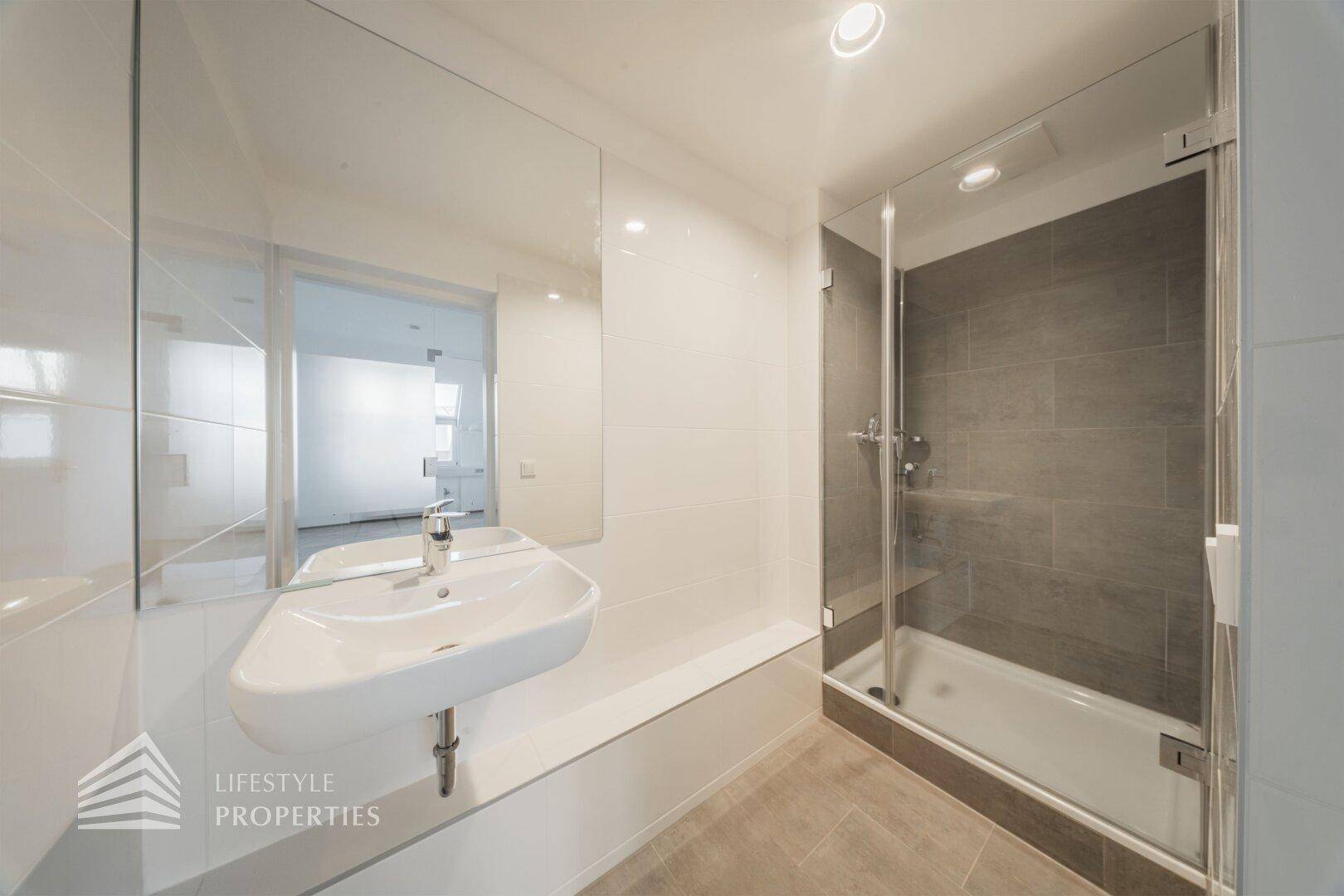 Modernes Badezimmer mit Duschkabine, Waschbecken, großem Spiegel und grauen Bodenfliesen.