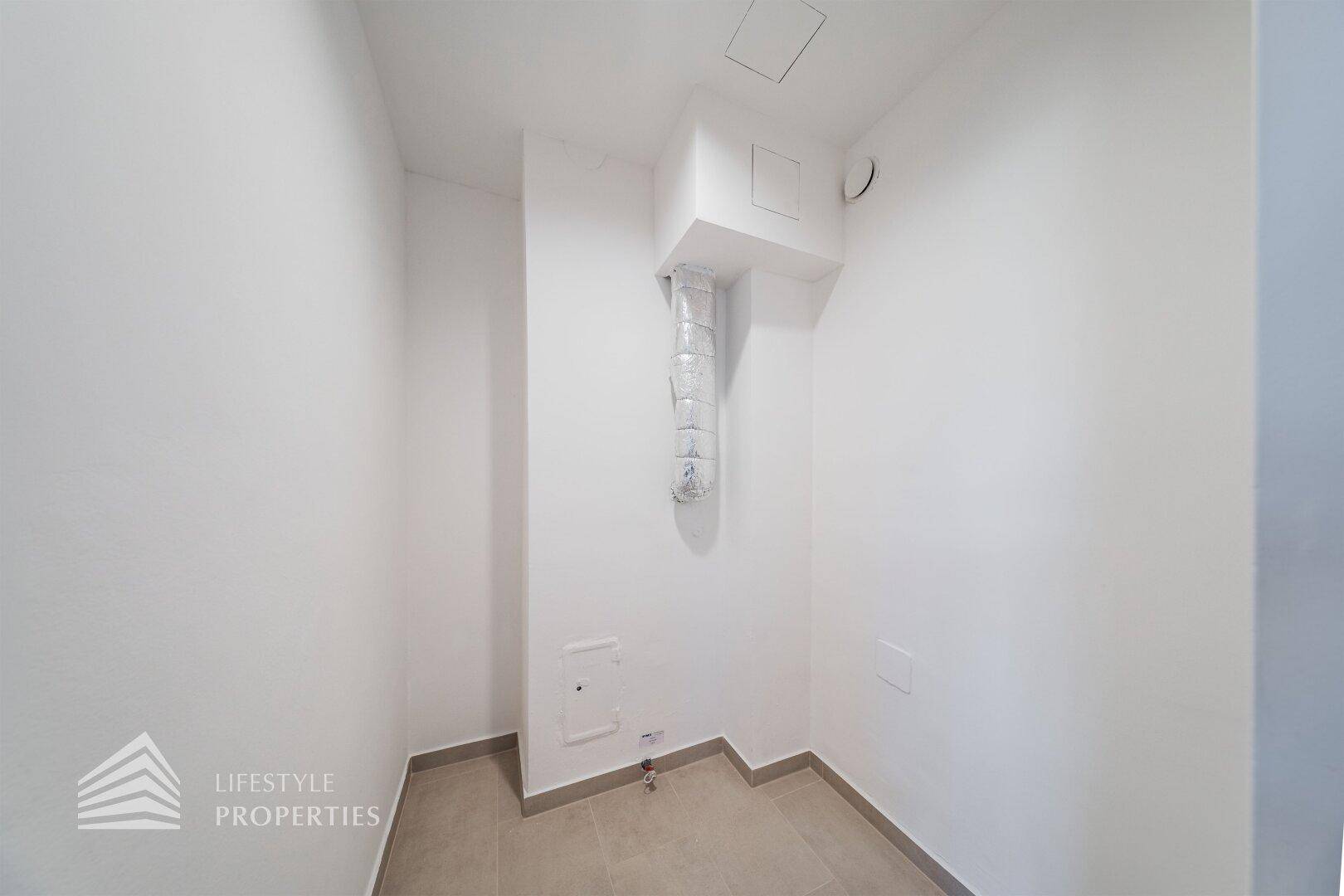 Kleiner Abstellraum mit Fliesenboden und sichtbarer Lüftungsanlage, ideal für technische Installationen.