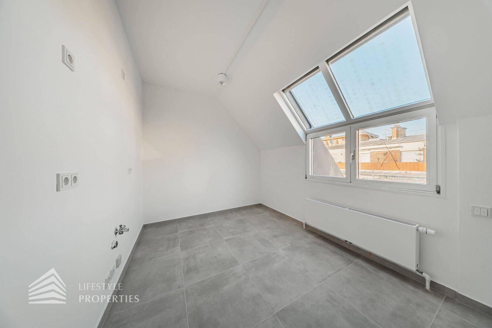 Kleiner Raum mit Fliesenboden, Dachfenster und sichtbaren Anschlüssen, möglicherweise für eine Teeküche.