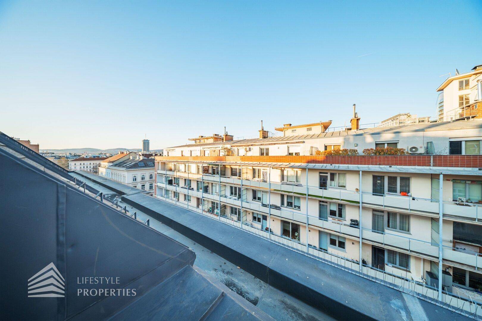 Weitläufiger Blick über die Dächer der Stadt mit angrenzenden Gebäuden und blauem Himmel.