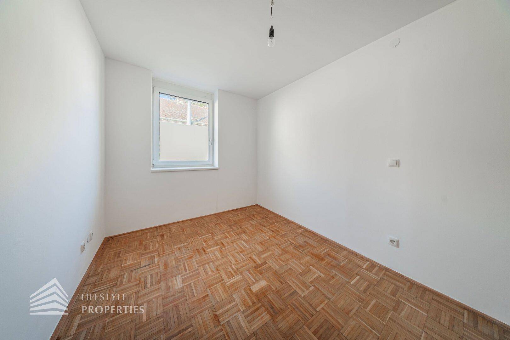 Ruhiges Zimmer mit Parkettboden und einem Fenster, das viel Tageslicht hereinlässt.