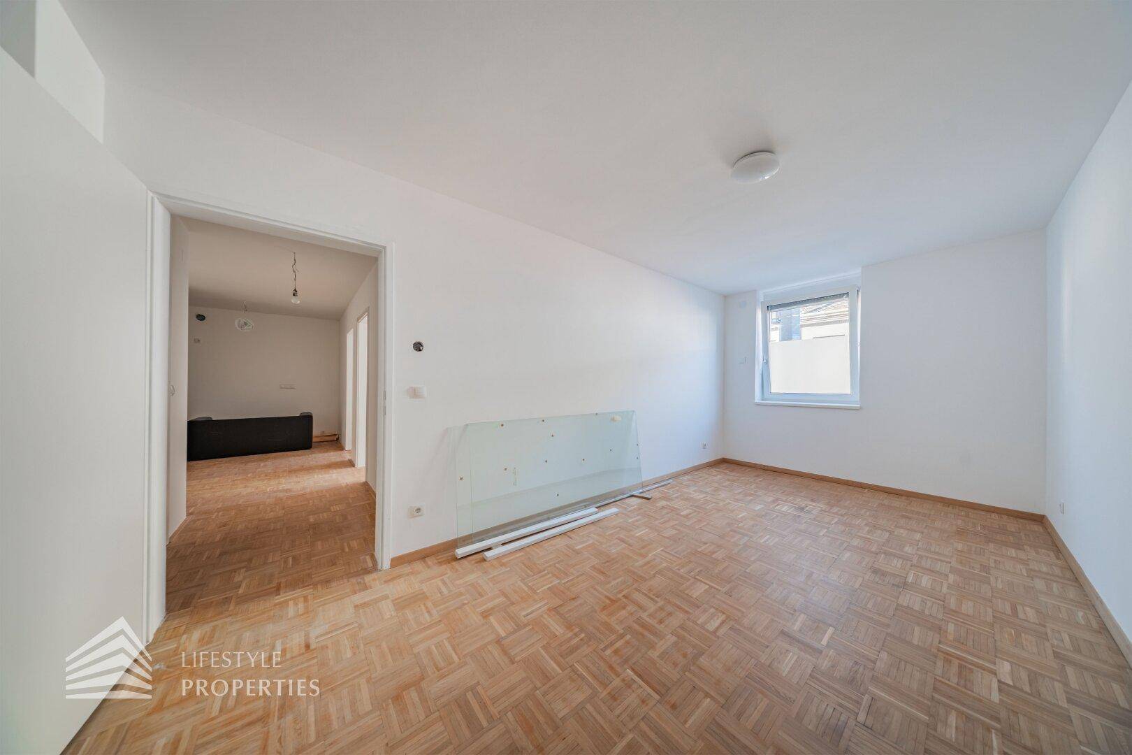 Geräumiger Wohnbereich mit Parkettboden und Zugang zu einem weiteren Zimmer.