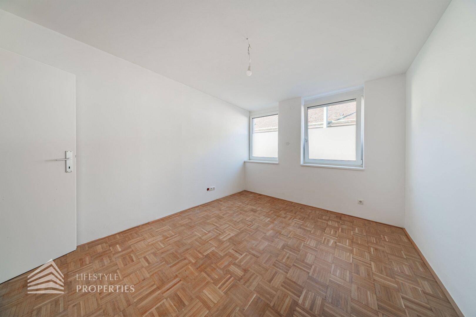Lichtdurchflutetes Zimmer mit Parkettboden und zwei Fenstern für optimale Belichtung.