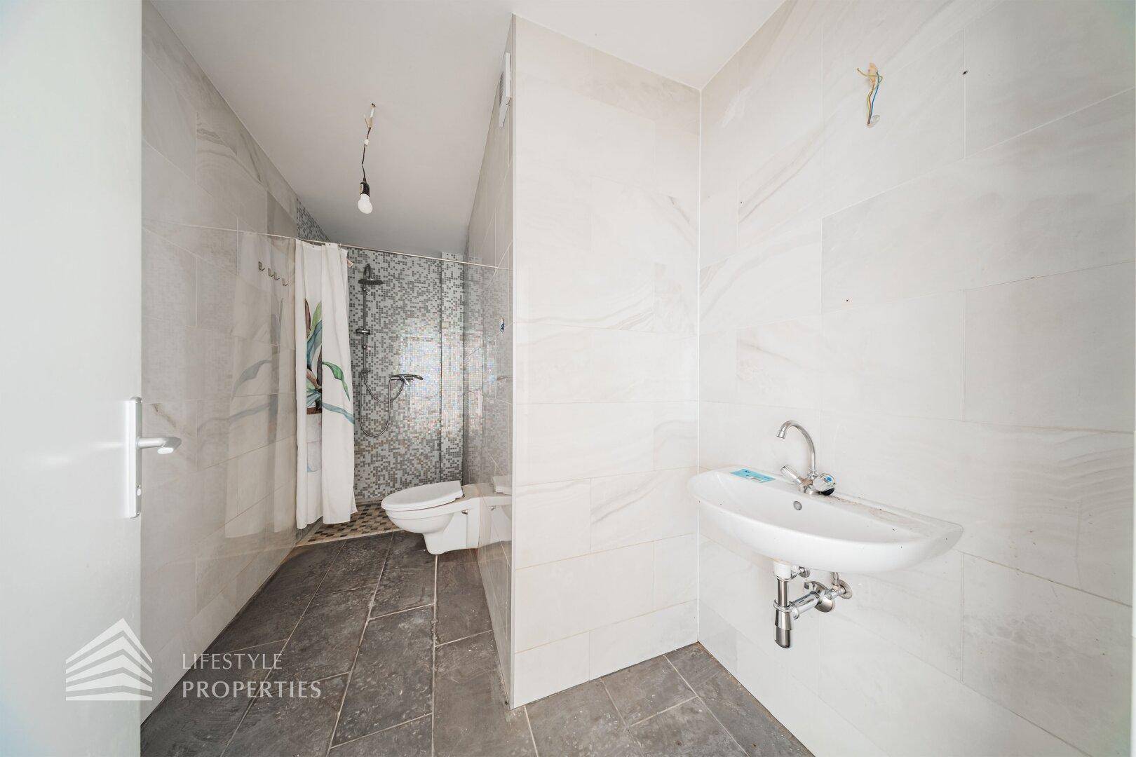 Modernes Badezimmer mit Dusche, WC und Waschbecken, ausgestattet mit hellen Fliesen.