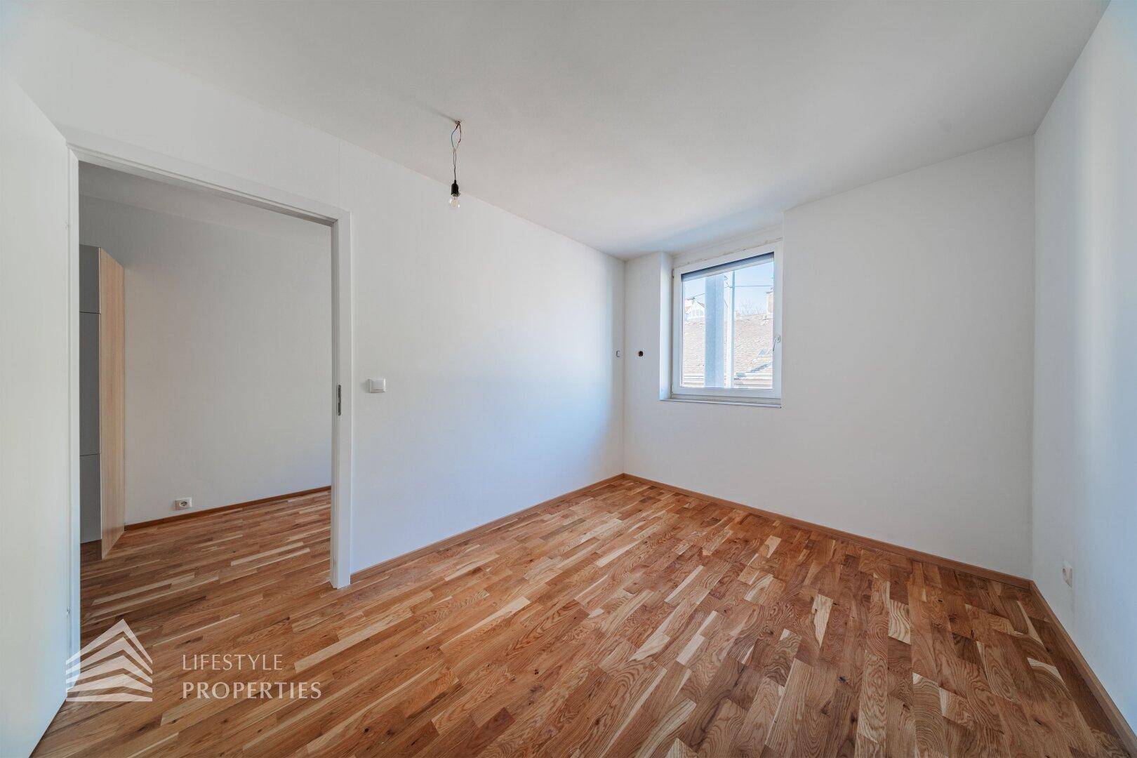 Helles Schlafzimmer mit Parkettboden, weißen Wänden und Fenster für Tageslicht.
