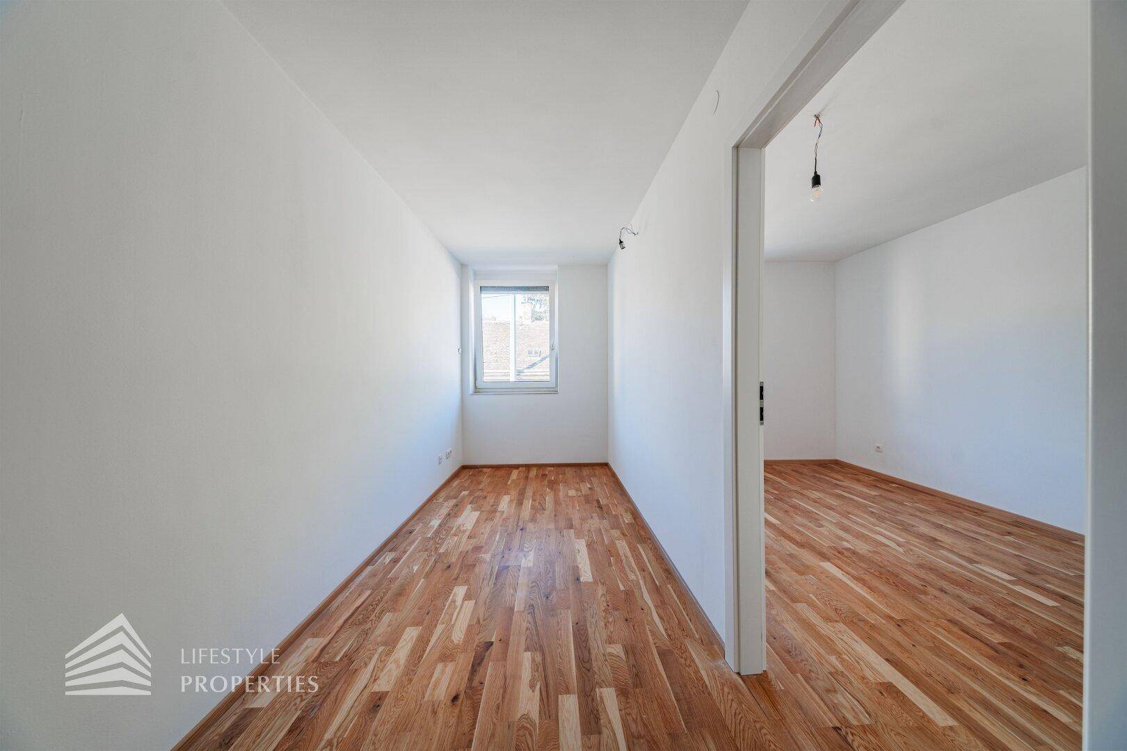Leeres Zimmer mit Holzboden und weiß gestrichenen Wänden, ideal als Schlaf- oder Arbeitszimmer.