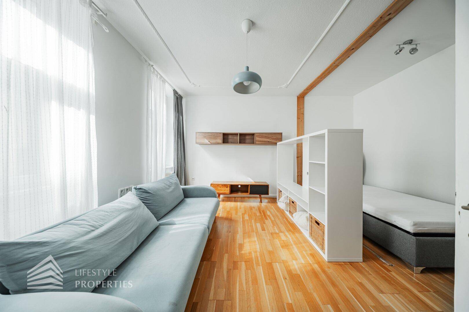 Lichtdurchfluteter Wohnbereich mit langem Sofa, Holzbalken und Parkettboden.