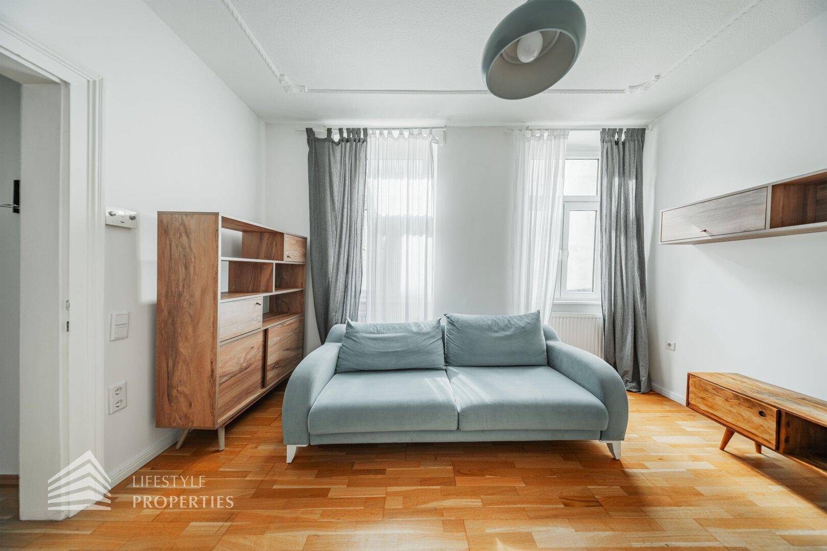 Gemütlicher Wohnbereich mit hellem Parkettboden, modernem Sofa und großen Fenstern.