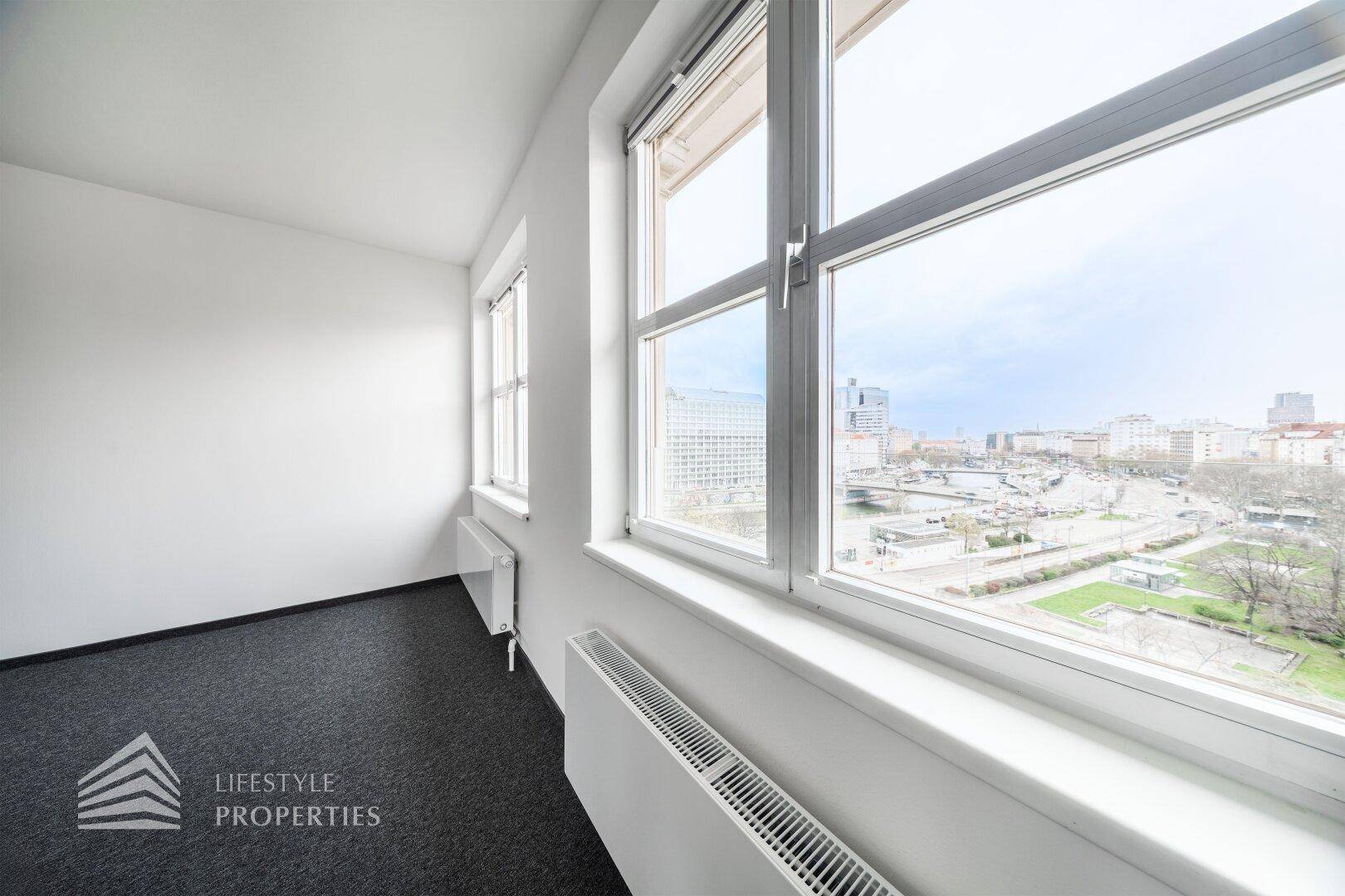 Heller Büroraum mit Teppichboden und großen Fenstern, die einen weiten Stadtblick bieten.