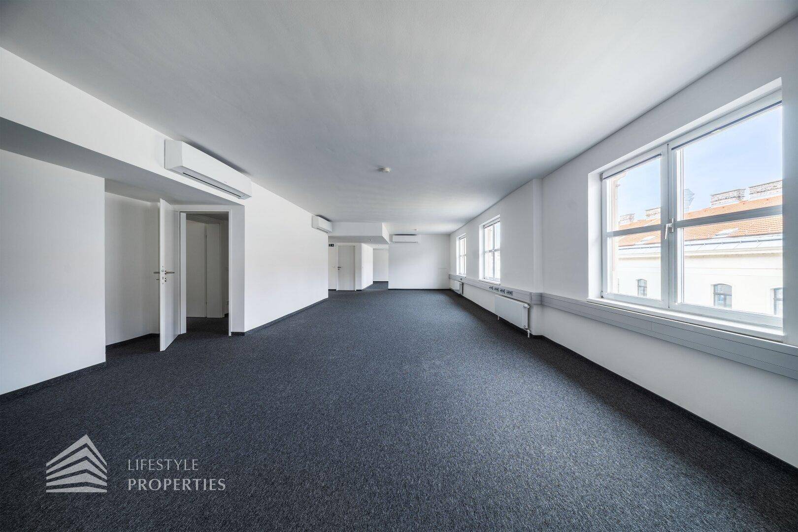 Heller Büroraum mit Teppichboden, mehreren Fenstern und integrierter Klimaanlage für angenehmes Arbeitsklima.