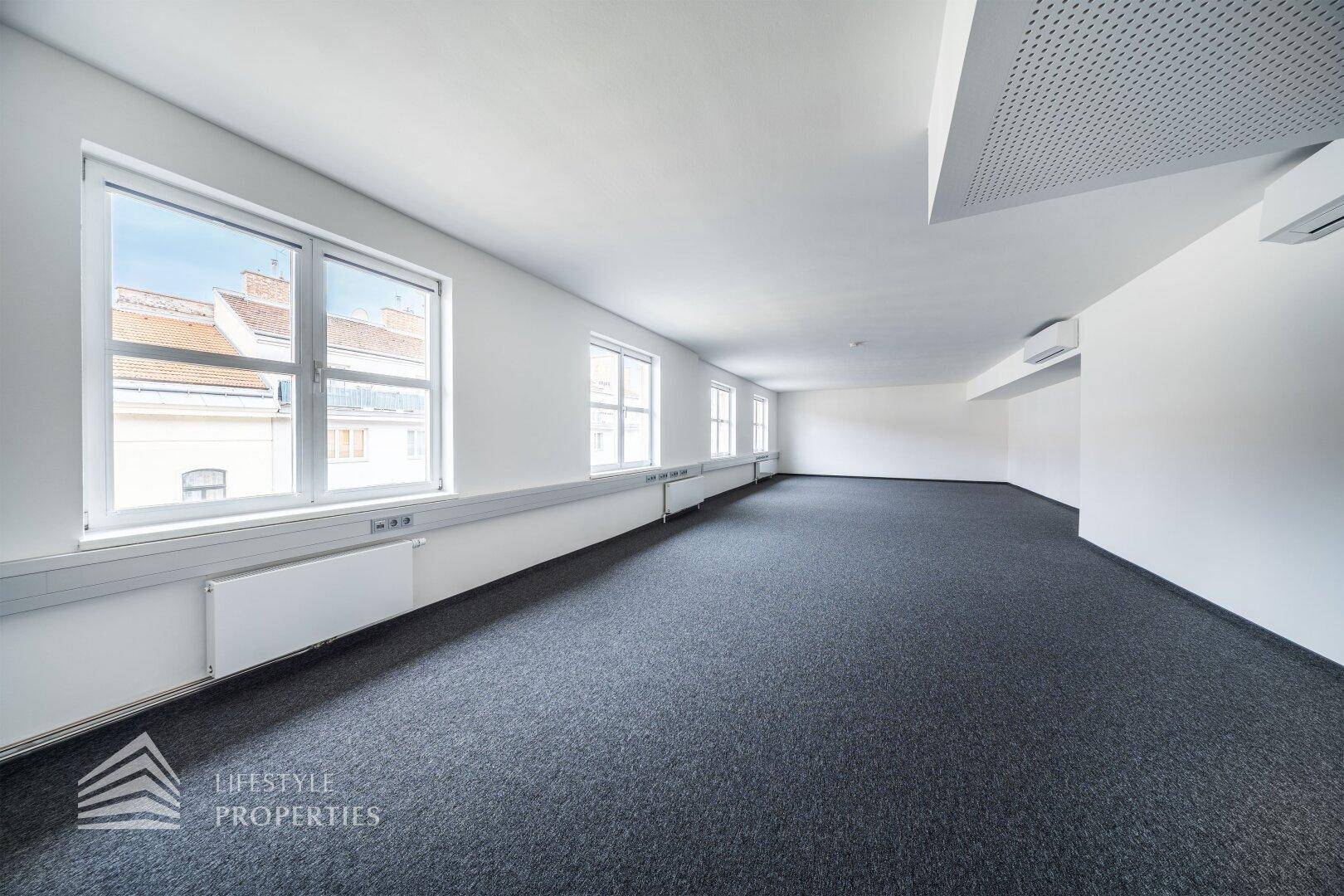 Geräumiger Büroraum mit Teppichboden, mehreren Fenstern und Klimaanlage, ideal für flexible Nutzung.