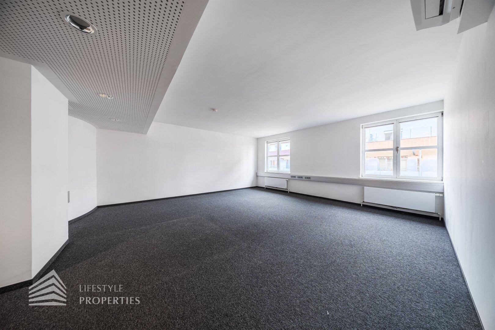 Heller Büroraum mit perforierter Decke, Einbauleuchten und Klimaanlage.