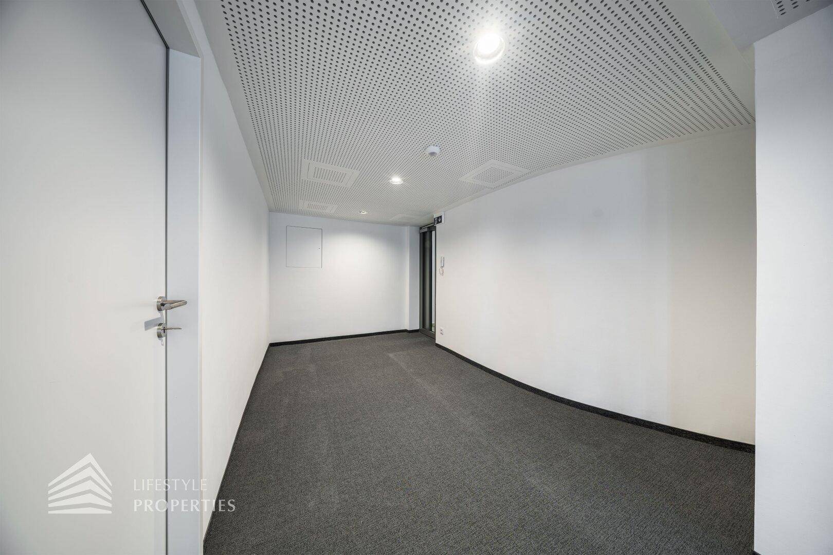 Flur oder kleinerer Bürobereich mit perforierter Decke und Einbauleuchten.