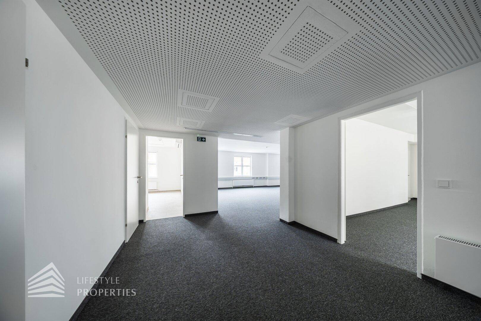 Flur oder Eingangsbereich eines Büros mit grauem Teppichboden und Zugang zu weiteren Räumen.