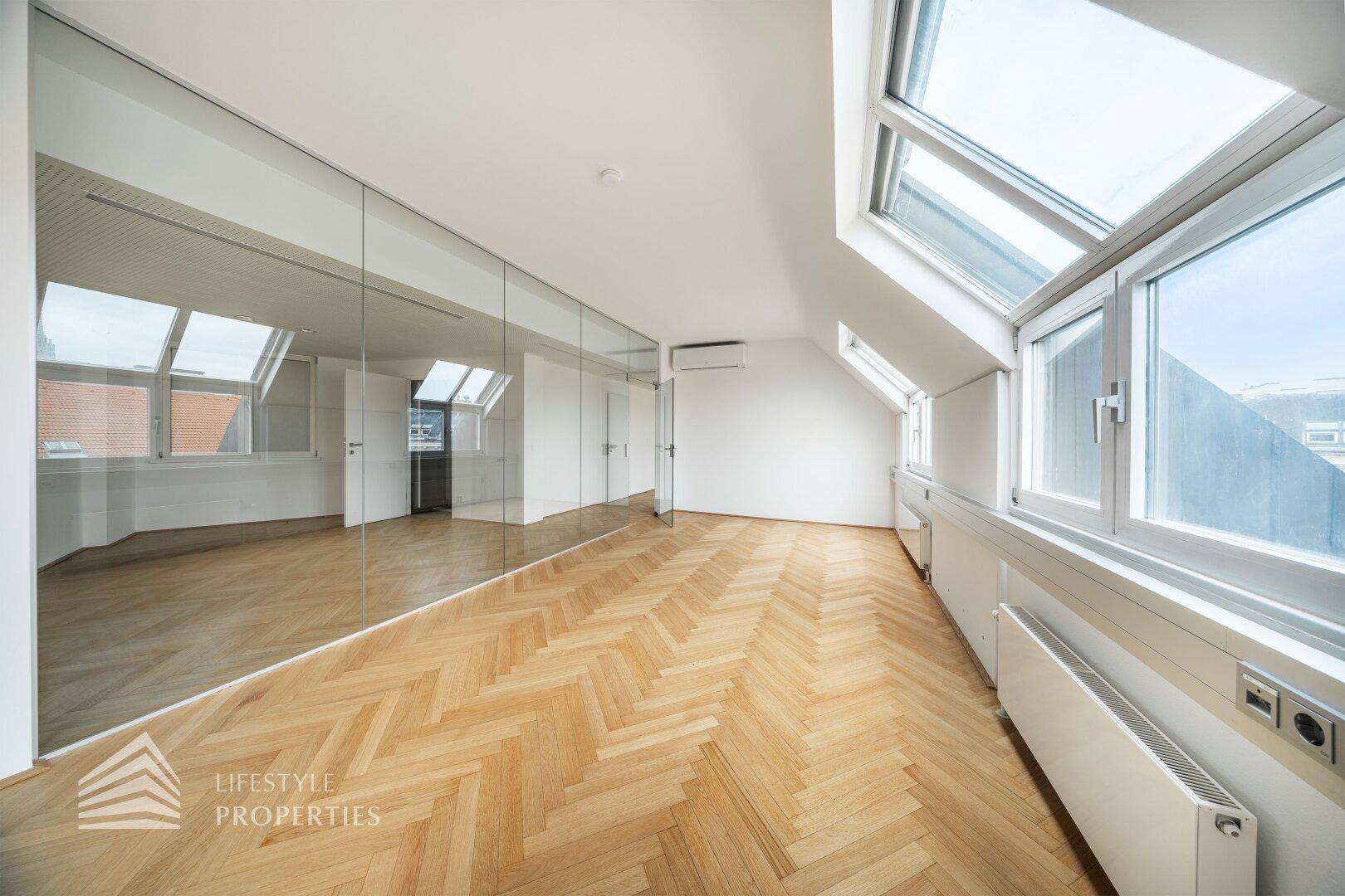 Modernes Büro mit schrägen Wänden, Fischgrätparkett und einer Klimaanlage, die für angenehme Temperaturen sorgt.
