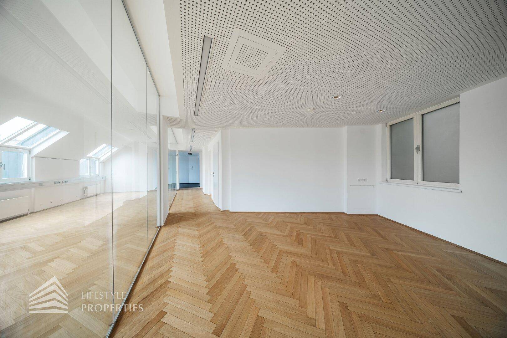 Heller Büroraum mit perforierter Decke, integrierter Beleuchtung und modernem Fischgrätparkett, ideal für konzentriertes Arbeiten.