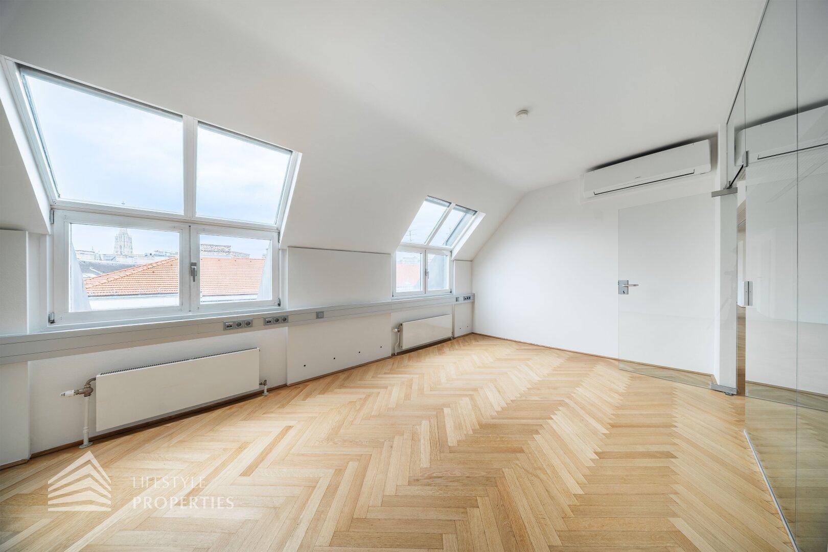 Heller Büroraum im Dachgeschoss mit schrägen Wänden, großen Fenstern und einer Klimaanlage für Komfort.