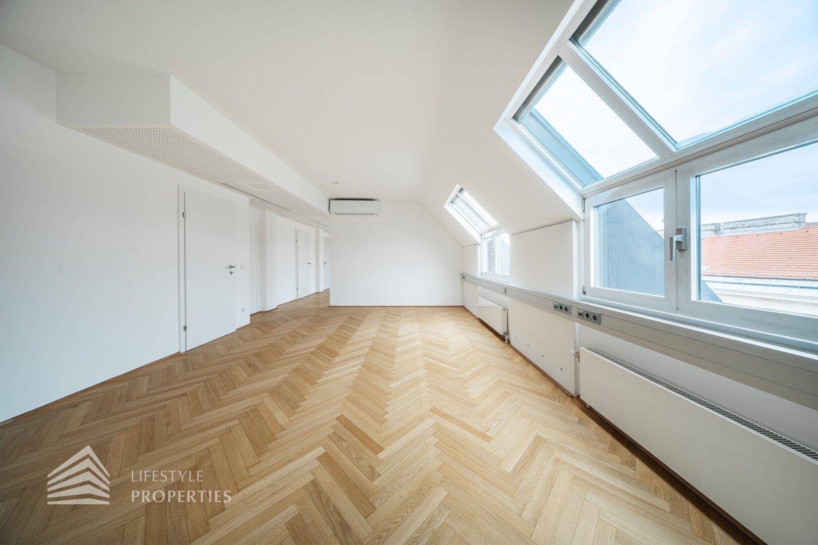 Großer Büroraum mit Fischgrätparkett, vielen Dachfenstern und weiß gestrichenen Wänden.