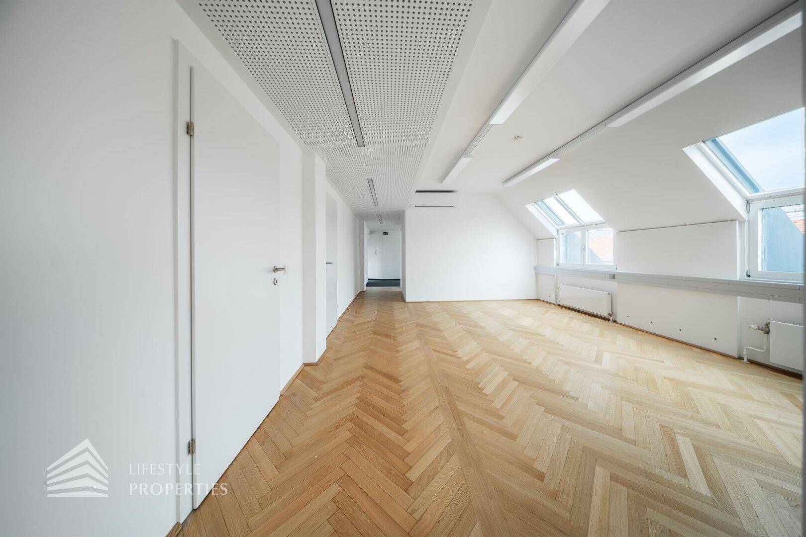 Geräumiger Bürobereich mit Fischgrätparkett, Dachfenstern und moderner Deckenbeleuchtung.