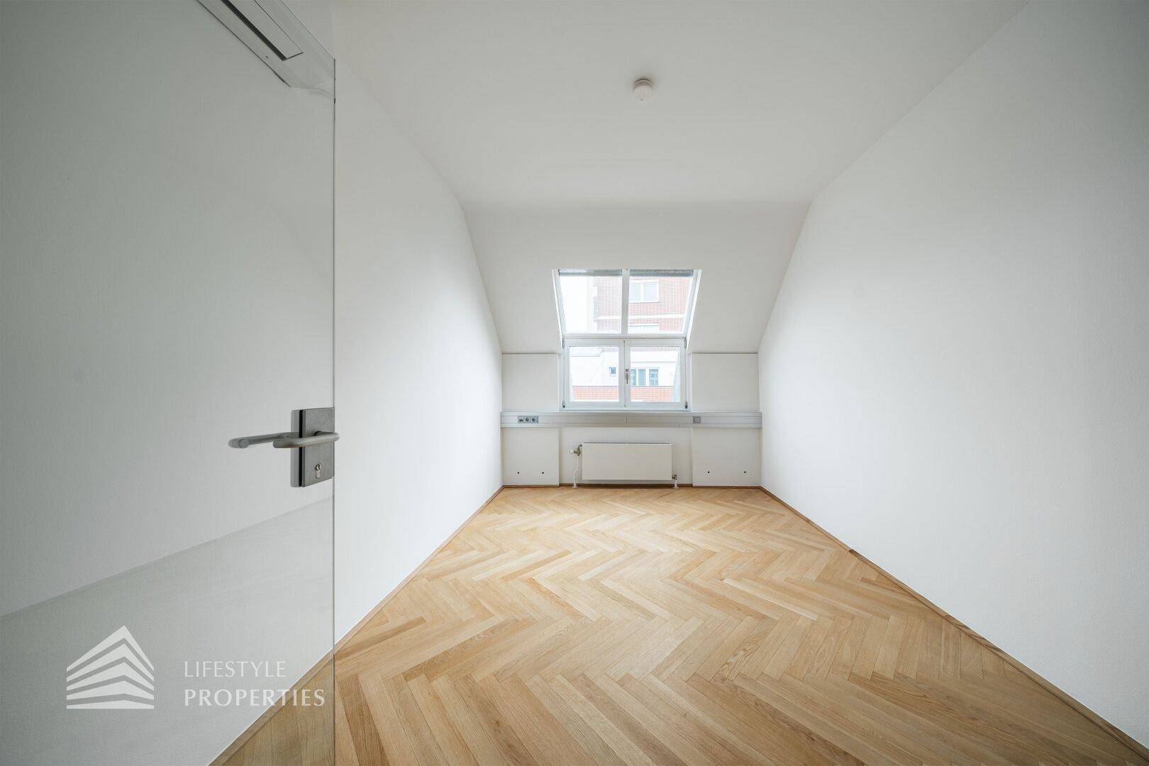 Kleiner Büroraum mit schrägem Dachfenster, Fischgrätparkett und weißen Wänden, ideal für konzentriertes Arbeiten.