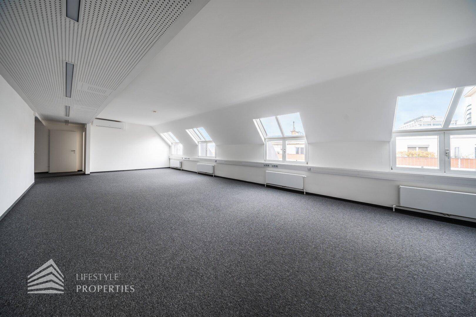 Großer, offener Büroraum im Dachgeschoss mit mehreren Dachfenstern und Teppichboden.