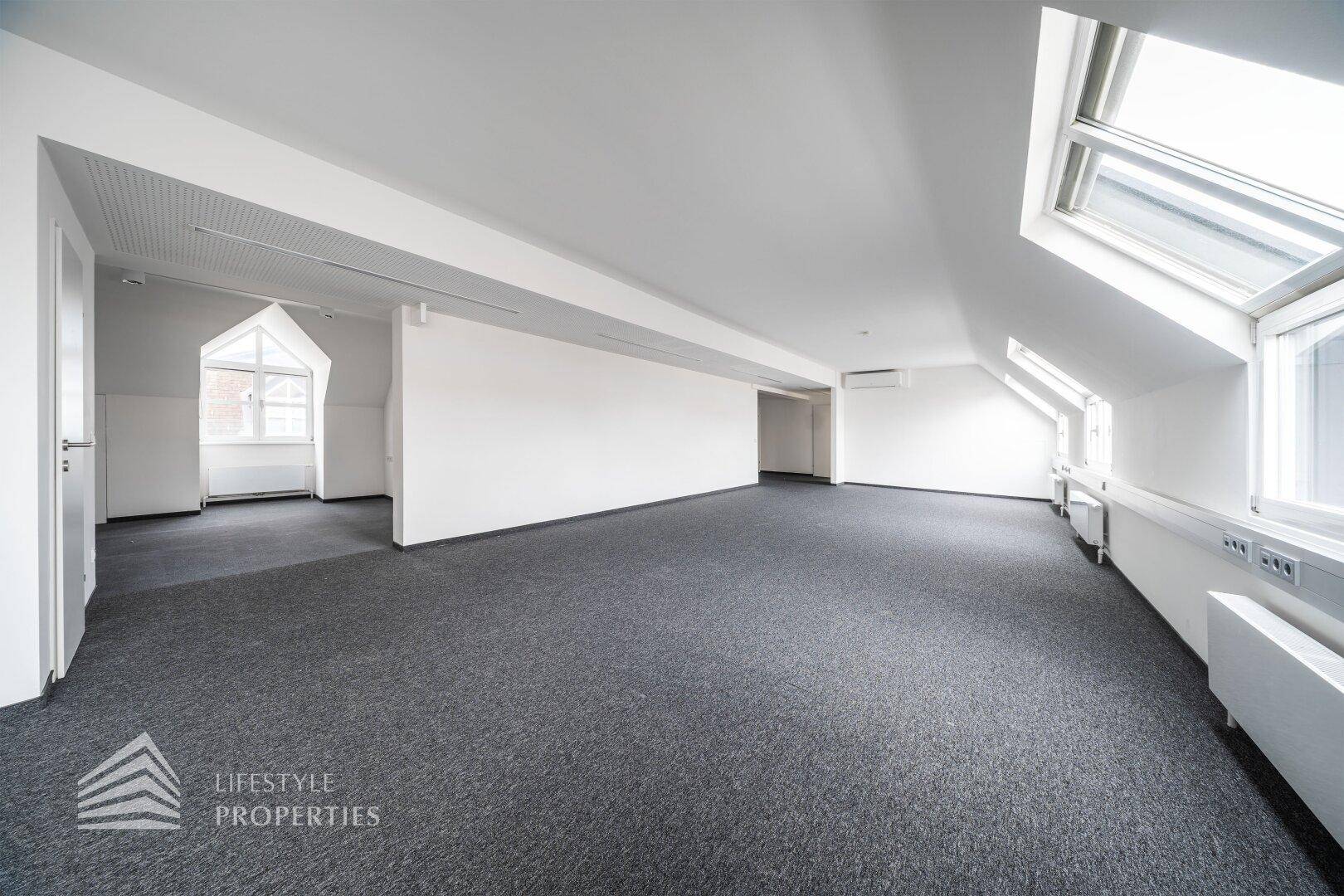 Offener Büroraum mit Teppichboden, schrägen Wänden und Blick auf weitere Bereiche.