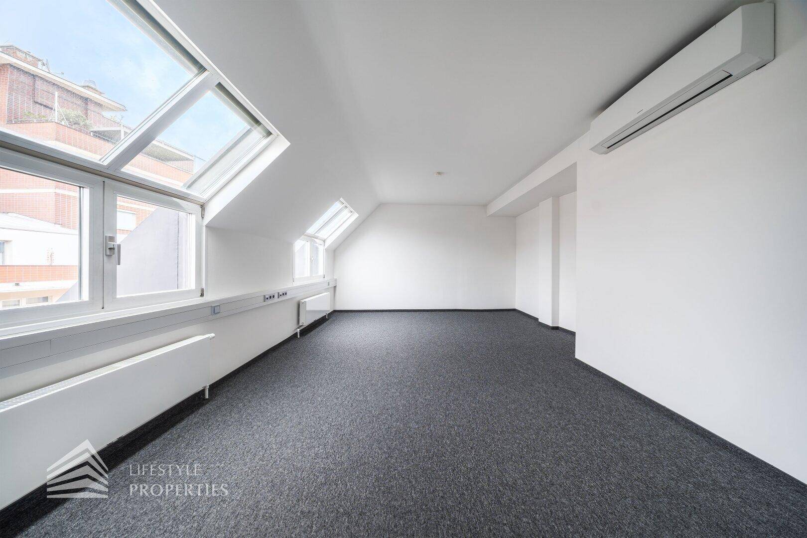 Heller Büroraum mit Klimaanlage, Teppichboden und großen Dachfenstern mit Stadtblick.