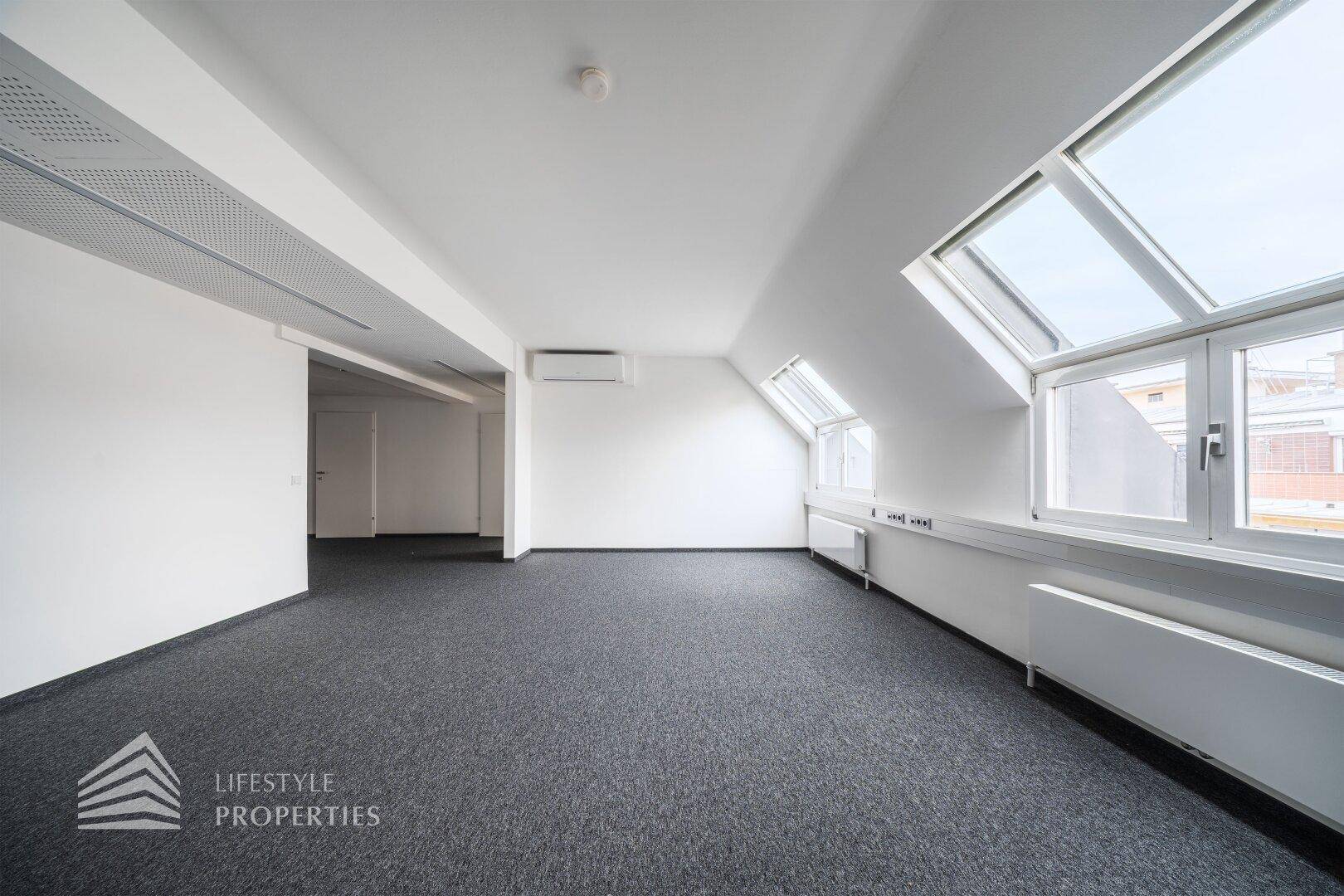 Moderner Büroraum mit Klimaanlage, Teppichboden und schrägen Wänden im Dachgeschoss.