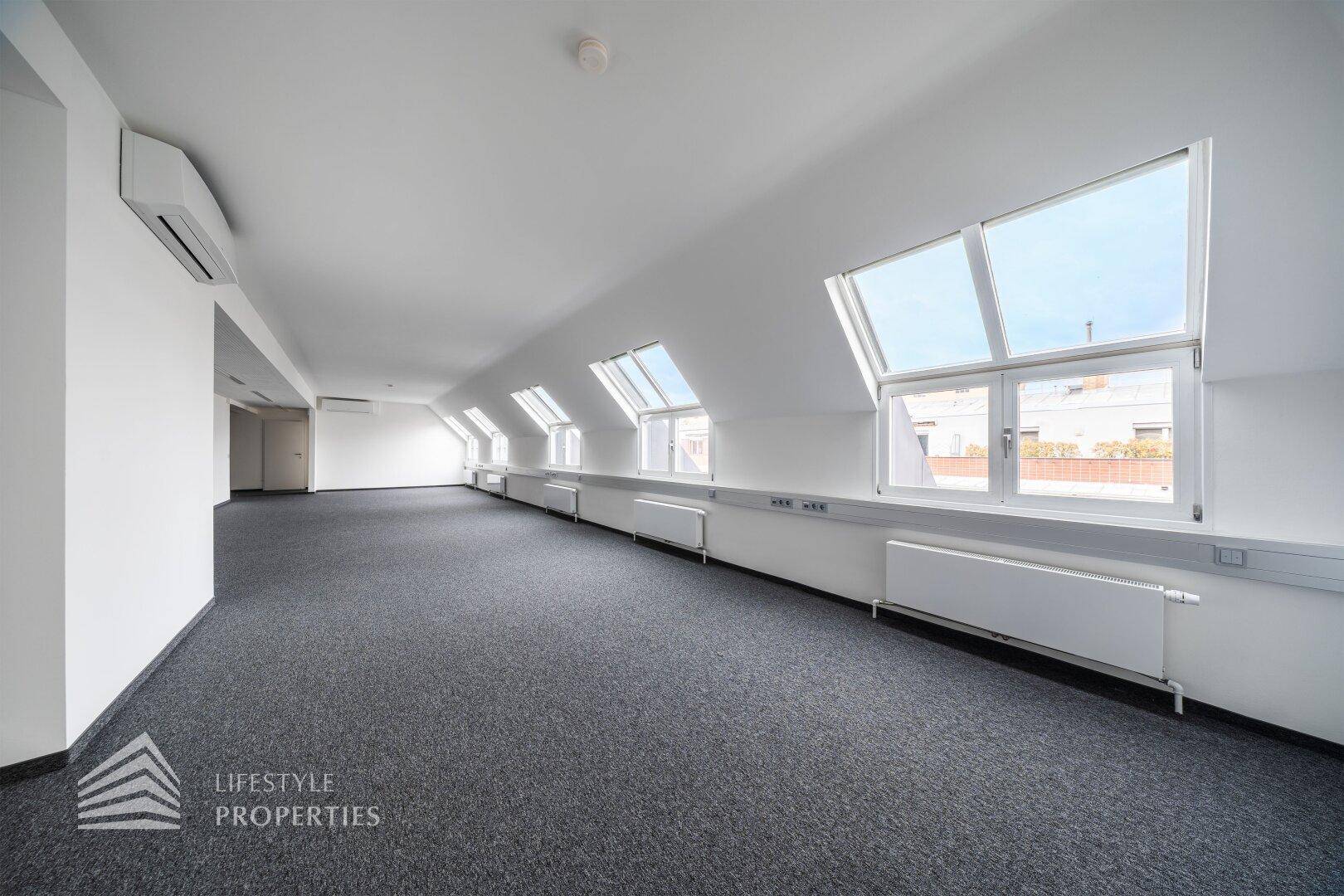 Geräumiger Bürobereich im Dachgeschoss mit vielen Fenstern und Teppichboden.