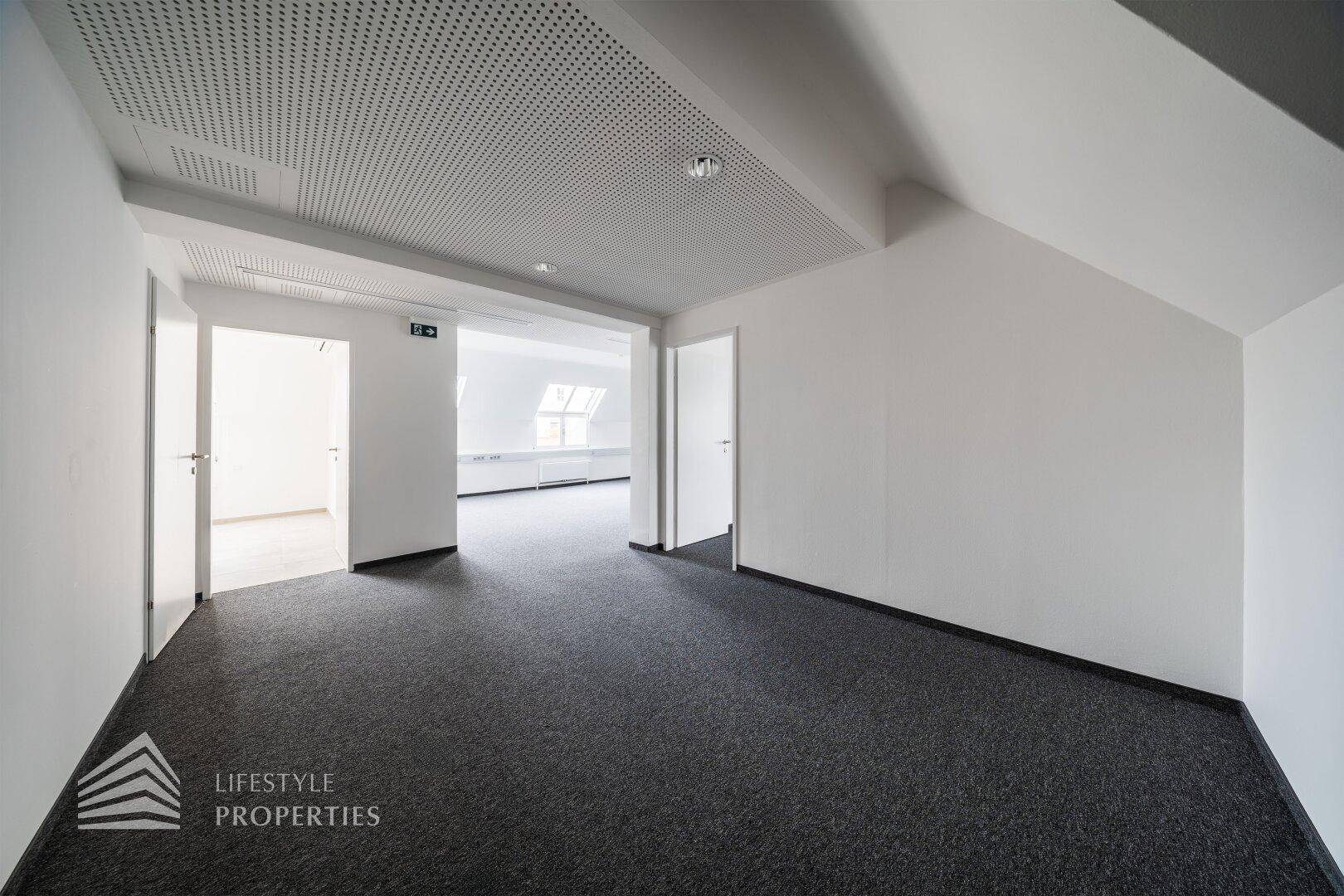 Büroflur mit Teppichboden und Zugang zu weiteren hellen Büroräumen im Dachgeschoss.