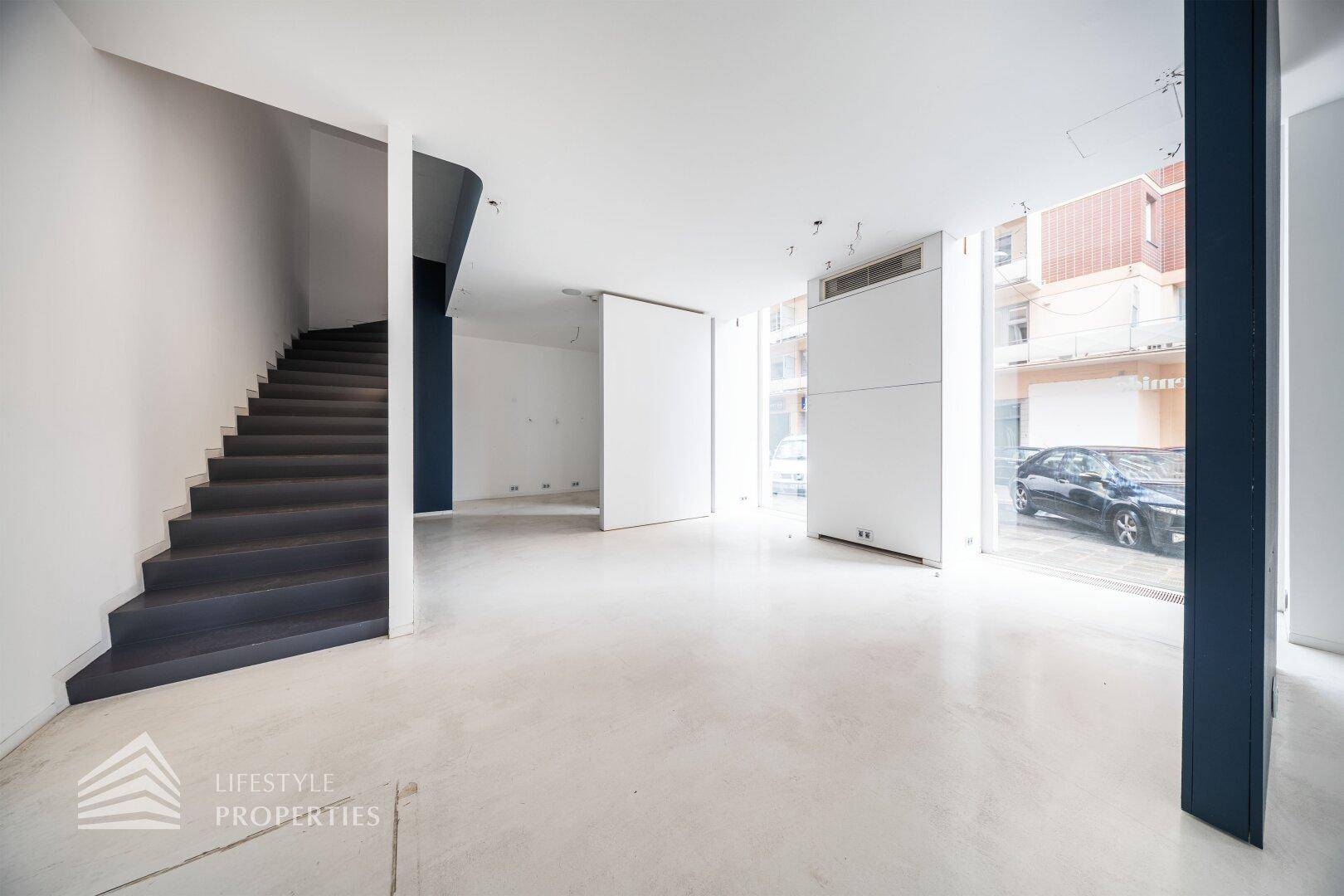 Heller Gewerberaum mit einer modernen Treppe und großen Fenstern zur Straße.