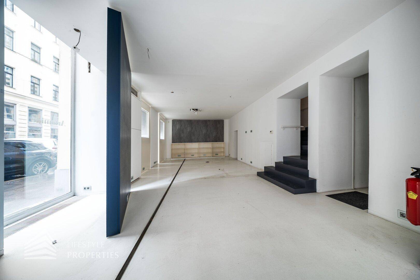 Weitläufiger Gewerberaum mit Treppe, großen Fenstern und einer dunklen Akzentwand.