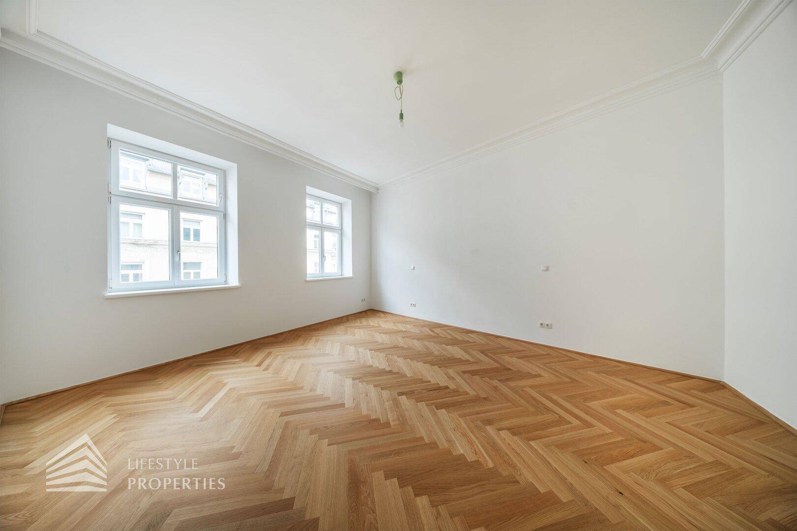 Geräumiges, helles Zimmer mit hohen Decken, zwei Fenstern und klassischem Fischgrätparkett.