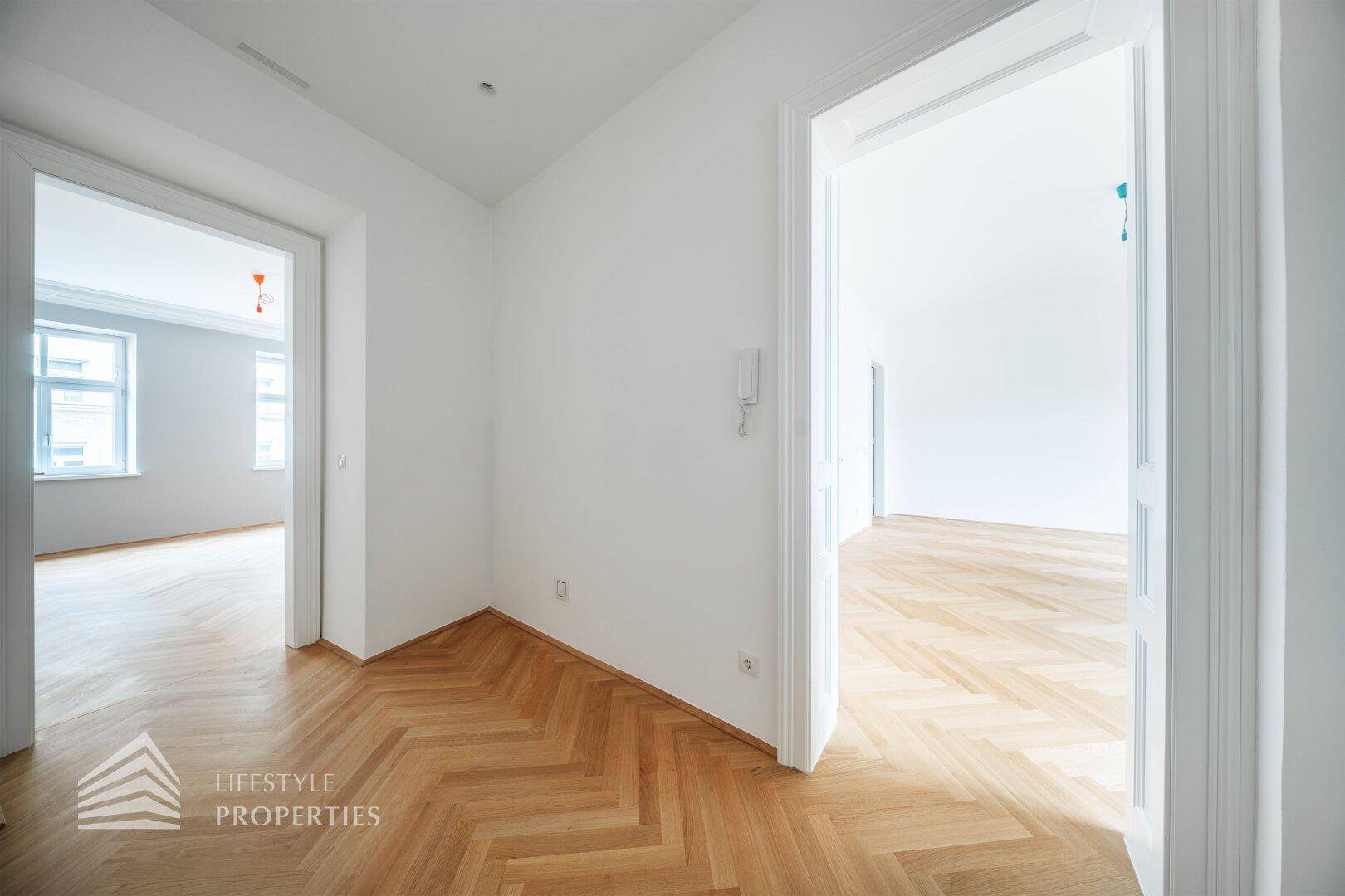 Heller Flur mit Fischgrätparkett und Zugang zu verschiedenen Zimmern der Wohnung.
