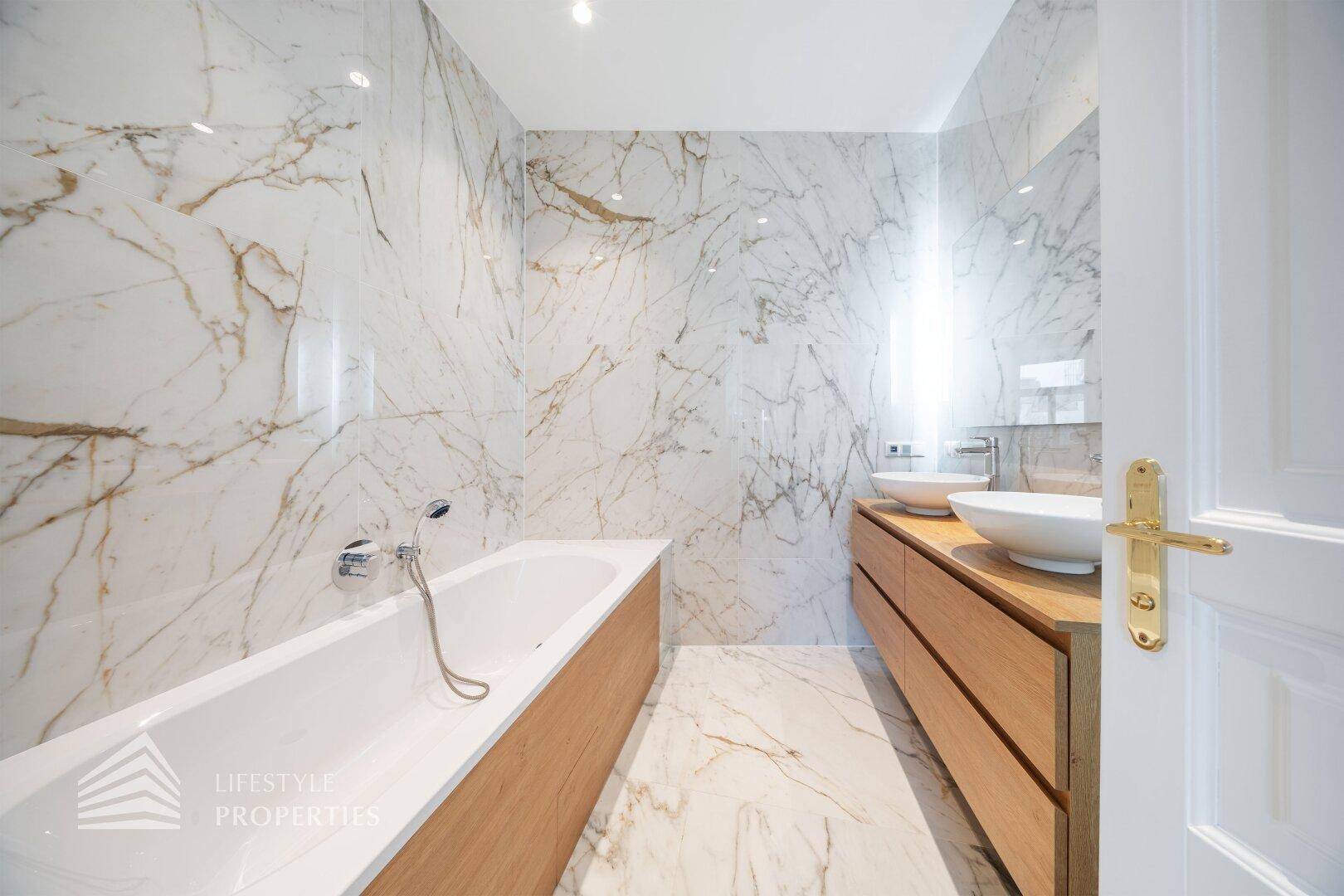 Luxuriöses Badezimmer mit Marmorfliesen, Doppelwaschbecken und integrierter Badewanne.