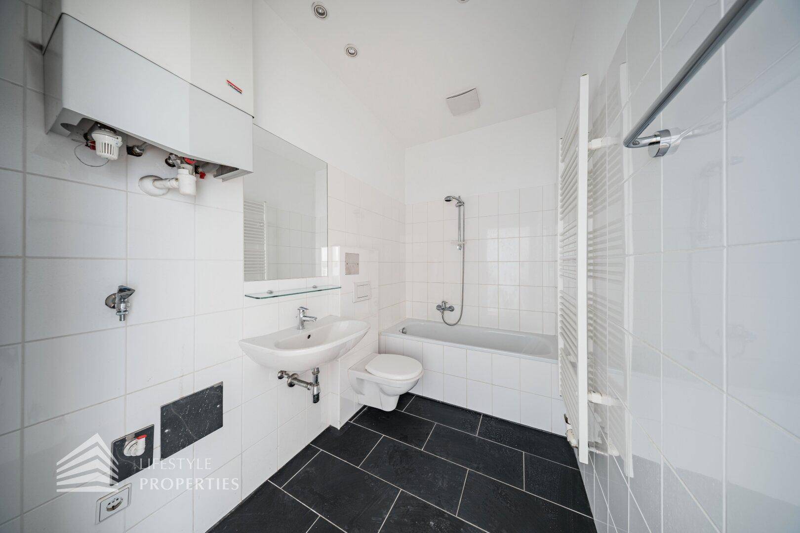 Helles Badezimmer mit Badewanne, Waschbecken und weißen Fliesen, ausgestattet mit Duschfunktion.