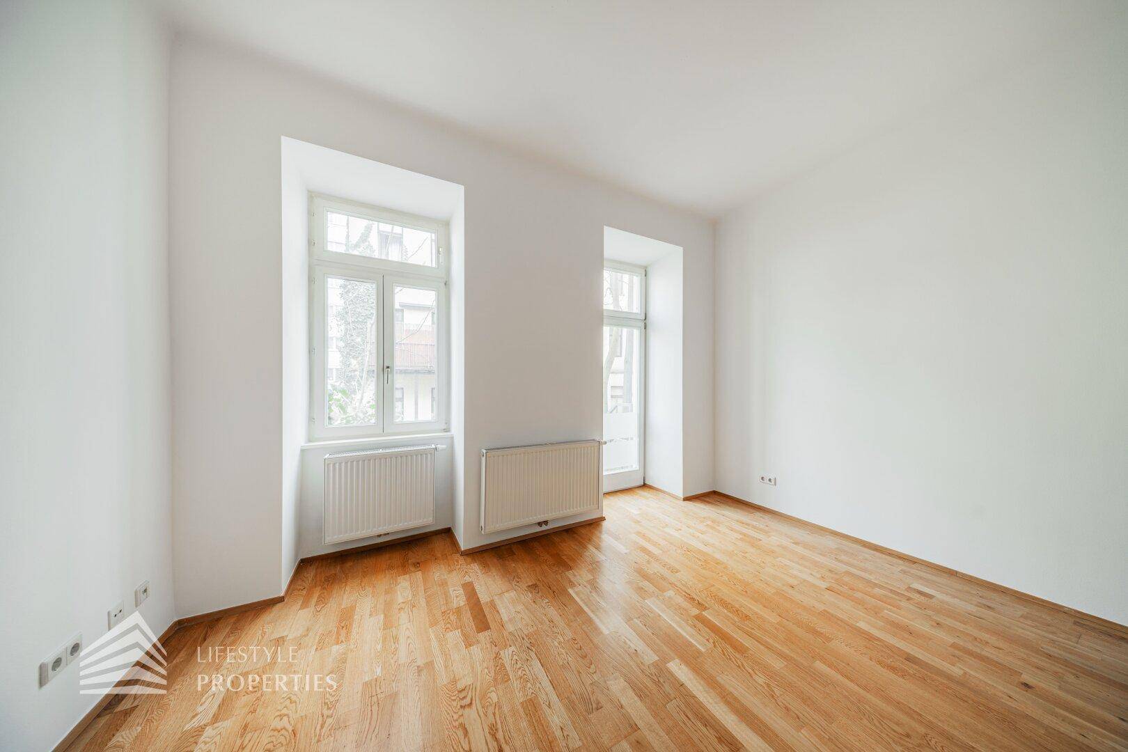 Geräumiger, heller Raum mit Parkettboden und hohen Fenstern, vielseitig nutzbar für Wohn- oder Schlafzwecke.