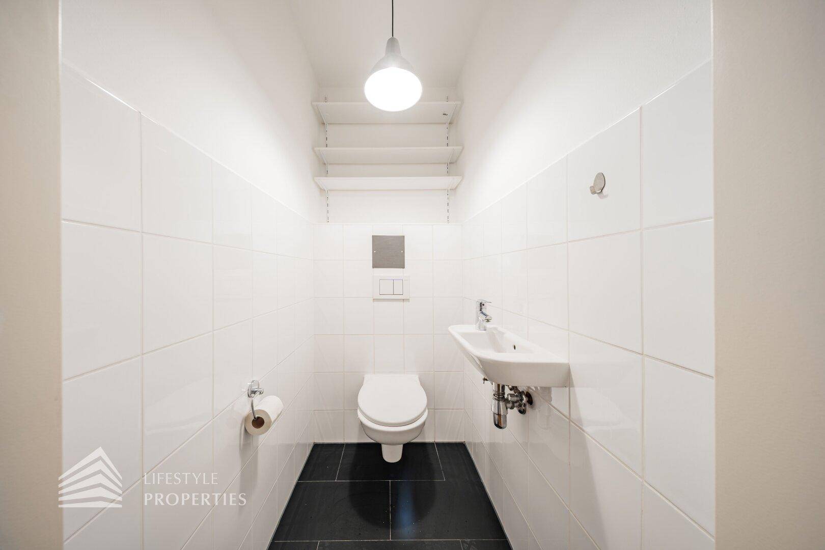 Modernes Gäste-WC mit wandhängender Toilette und dunklen Bodenfliesen, praktisch und platzsparend.