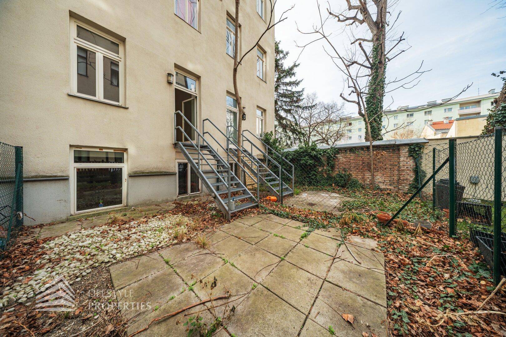 Unmöblierter Gartenbereich mit Steinplatten und Zugang zum Gebäude, bereit zur individuellen Gestaltung.