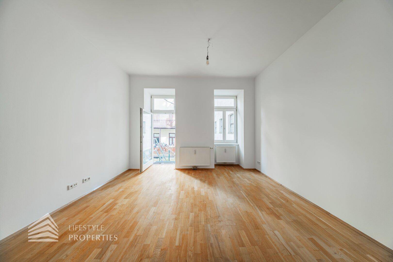 Geräumiger, heller Raum mit Parkettboden und Zugang zu einem französischen Balkon, ideal für viel Licht.