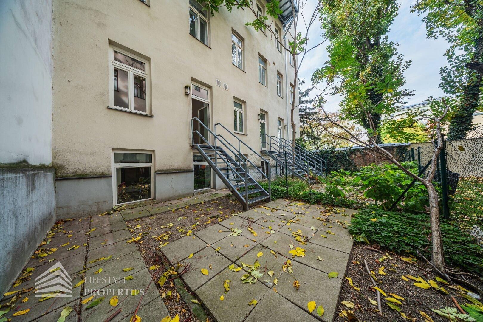 Unmöblierter Gartenbereich mit Steinplatten und Zugang zum Gebäude, bereit zur individuellen Gestaltung.