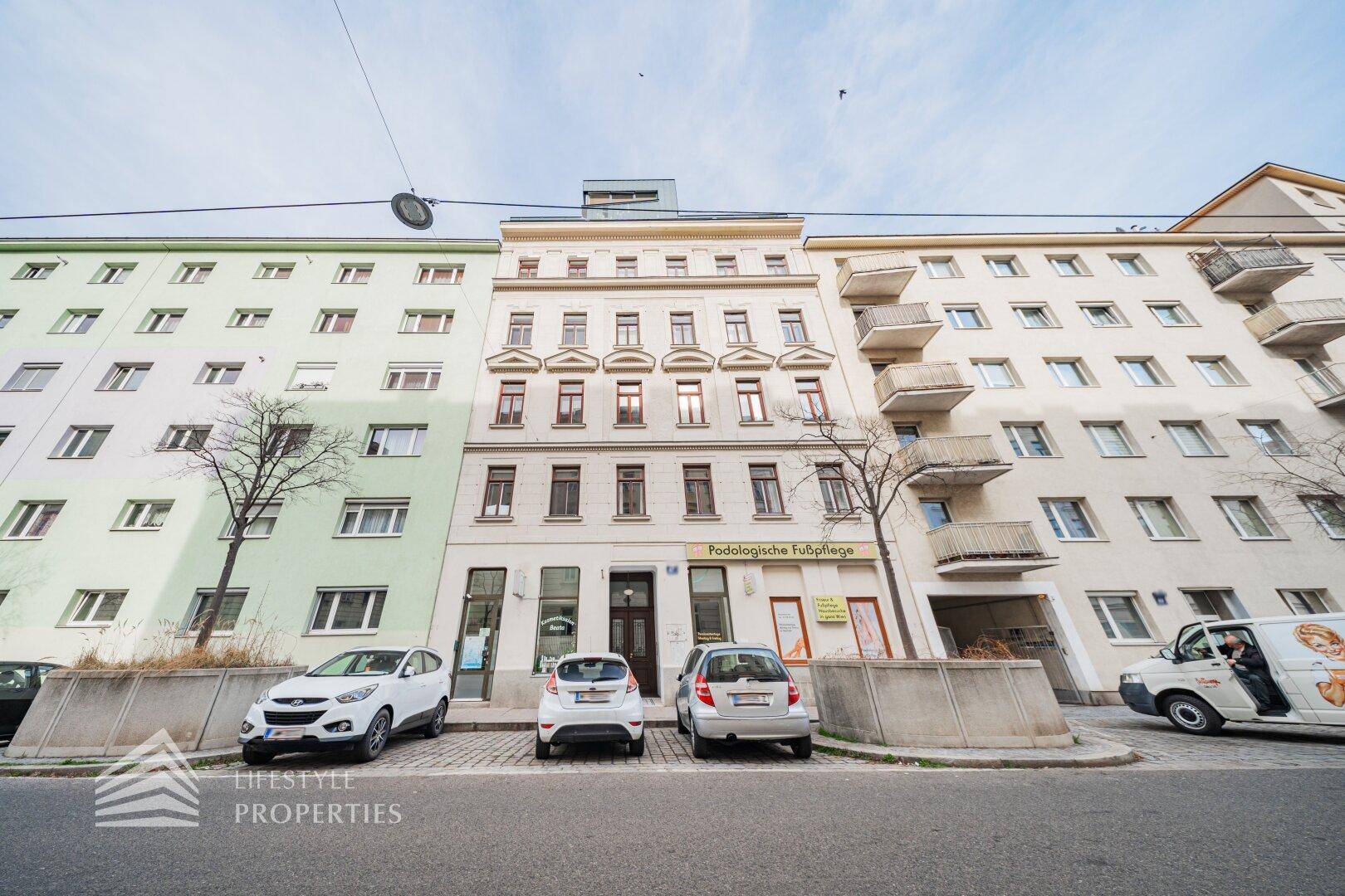 Historisches Gebäude mit Geschäften im Erdgeschoss und parkenden Autos auf der Straße.