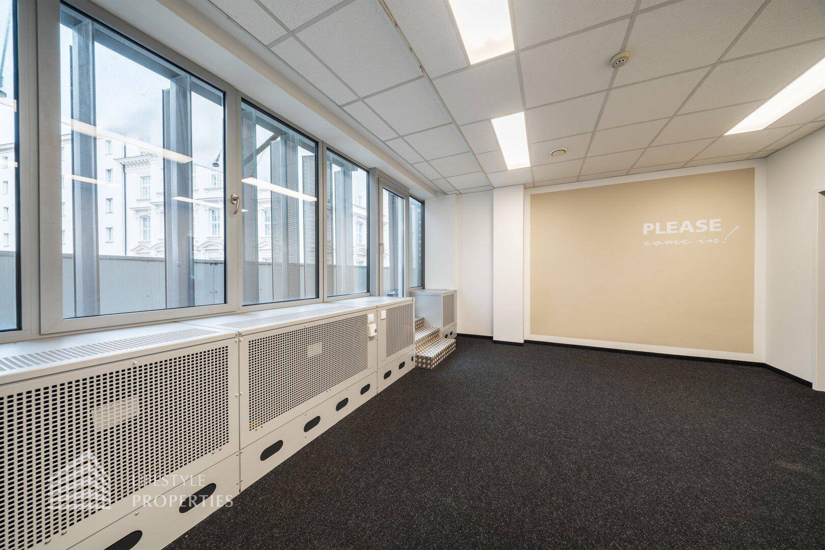 Heller Büroraum mit großen Fenstern, die einen weiten Blick bieten, und einer beigen Akzentwand.