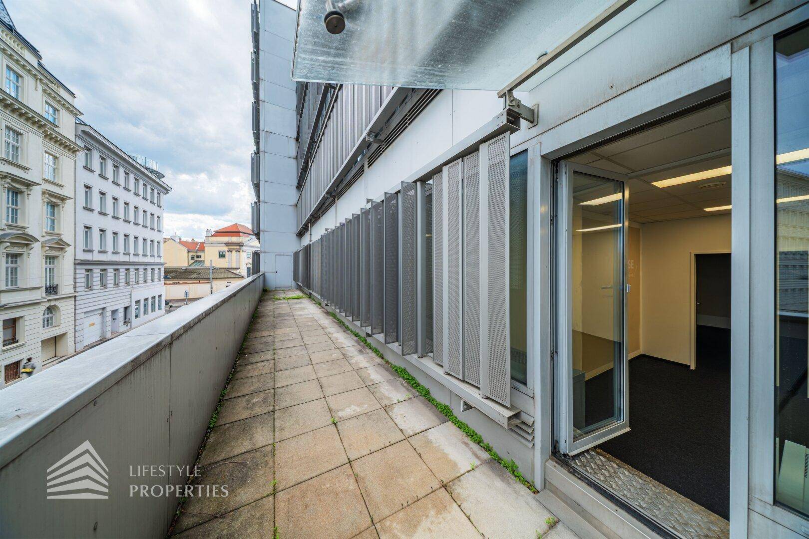 Lange Außenterrasse mit Steinplatten und Blick auf die umliegenden Stadtgebäude.